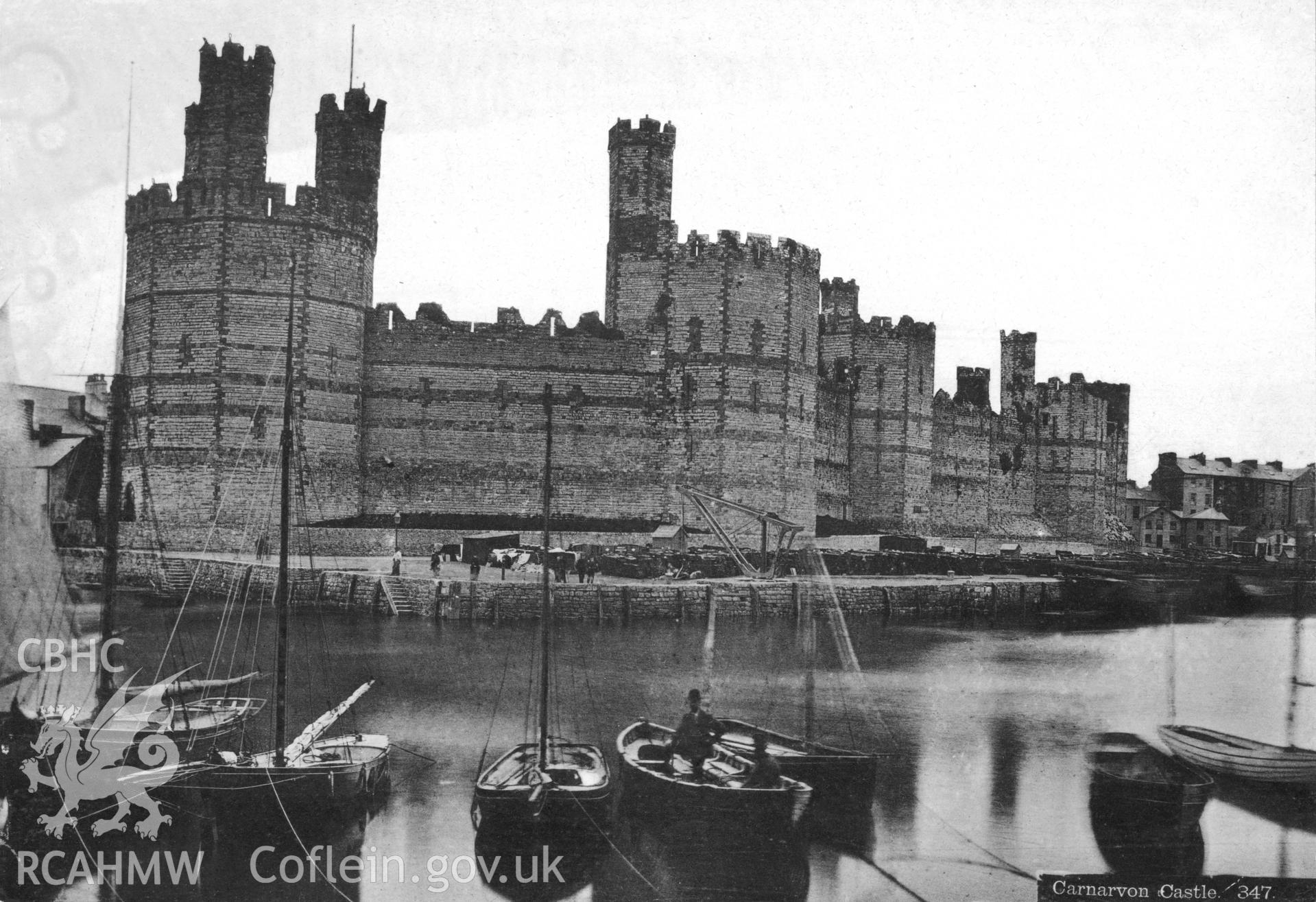 Undated black and white photograph of Caernarfon Castle, also visible in the background are the steps of the ferry and to the fore is the ferry with ferryman onboard alongside other rowing and sailing craft.