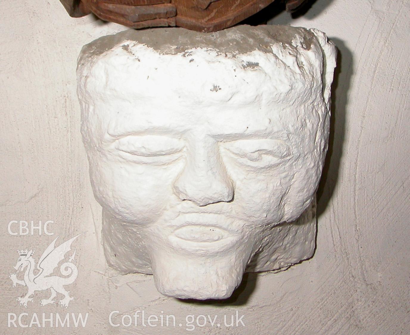 Carved stone head at east end, central.