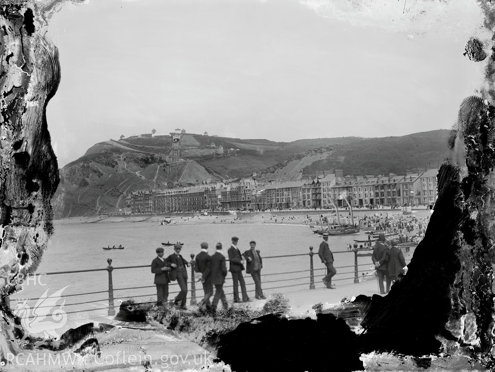 Black and white image dating from c.1910 showing a view of a busy beach and promenade at Aberystwyth taken from the castle side,  taken by Emile T. Evans.