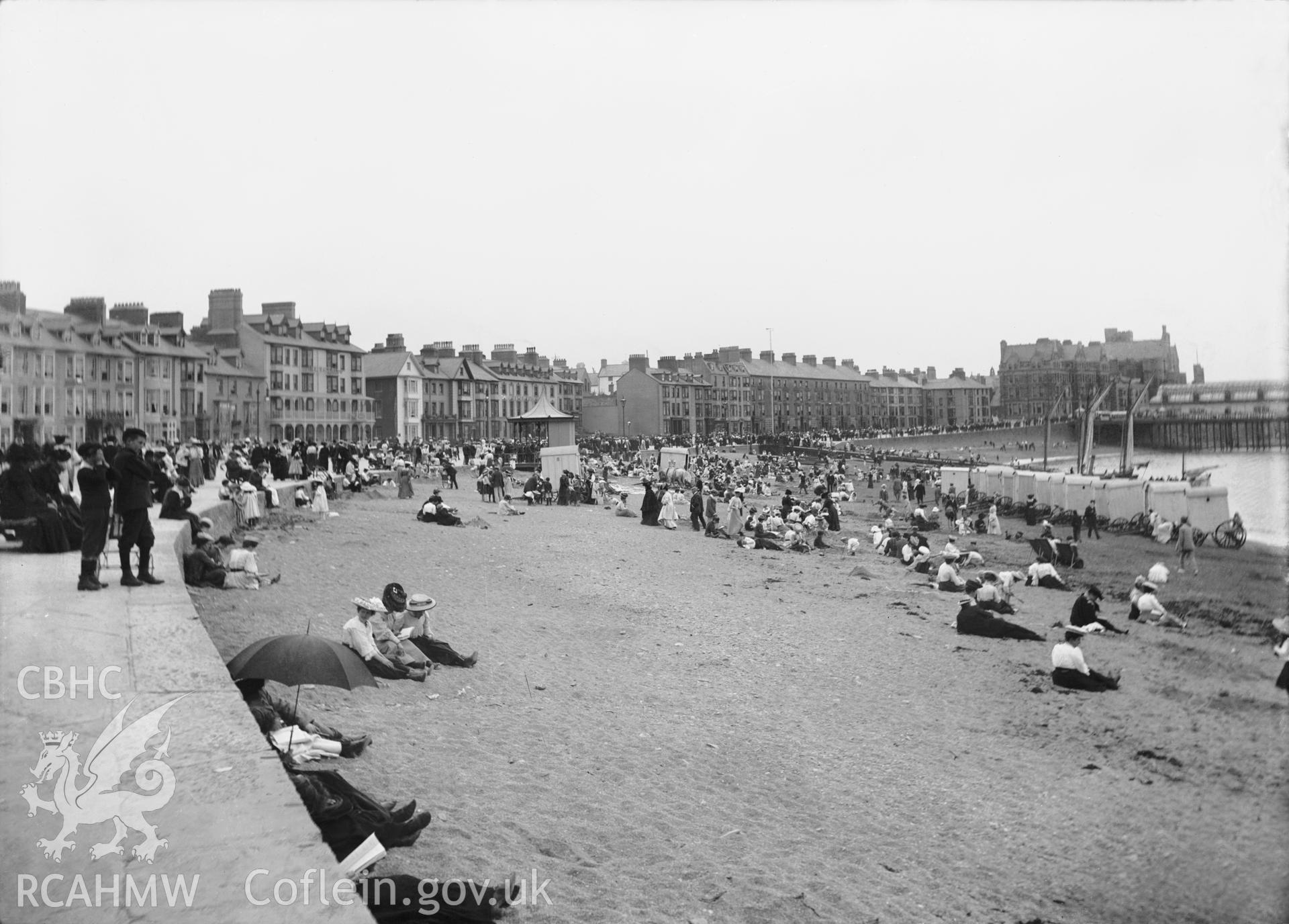 Black and white image dating from c.1910 showing a busy beach scene at Aberystwyth with Marine Terrace in the background.