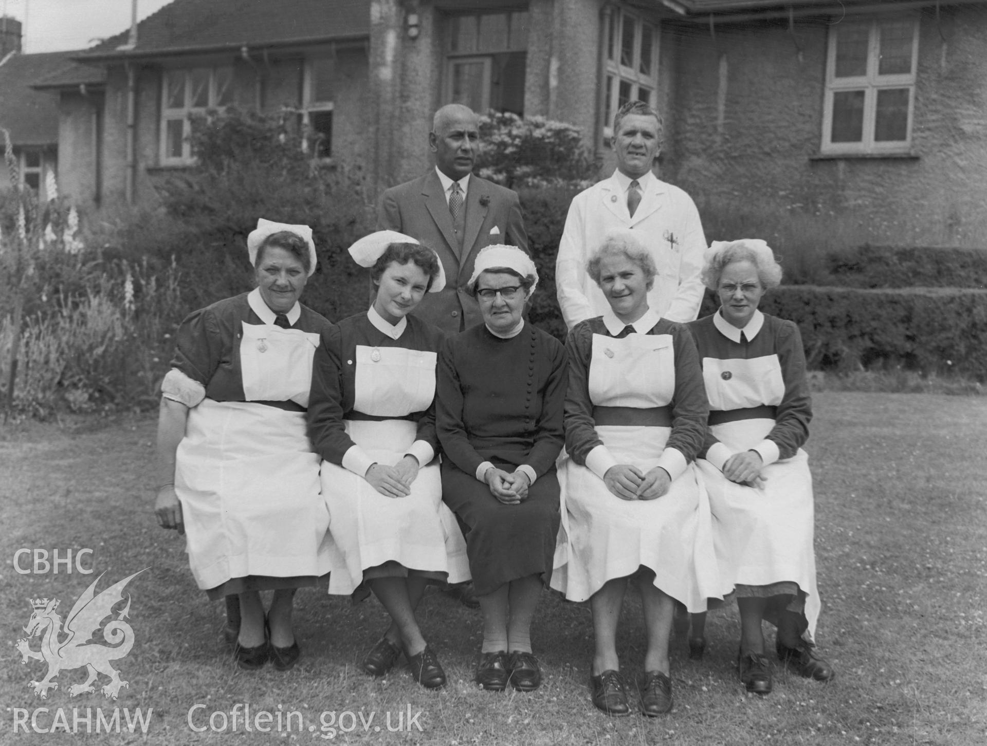 Black and white photograph showing medical staff outside Abertillery Hospital. Staff are identified as Dr R.W. Scanlon, Mr Aubrey (charge nurse), Sister Morgan or Sister Stevens, Sister Prosser, Matron G.E. Body, Sister Lewis and Sister Poultney.