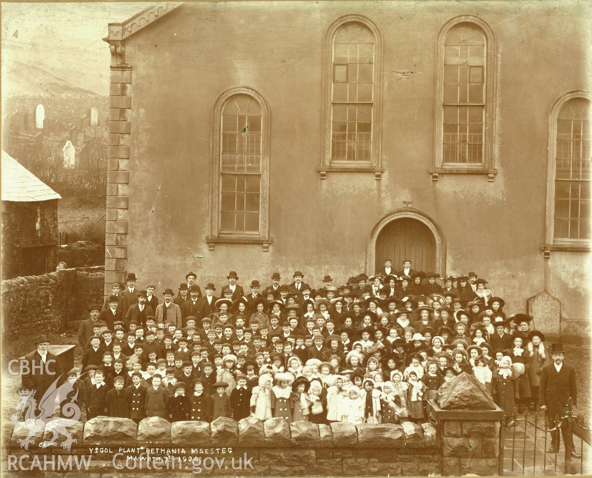 Digitized copy of a black and white photograph showing an exterior view of Bethania Chapel, Maesteg, with the congregation and school pupils. Part of a collection of material relating to Bethania Chapel, Maesteg, loaned for copying by the Welsh Religious Buildings Trust. The original collection is held by the Glamorgan Record Office.