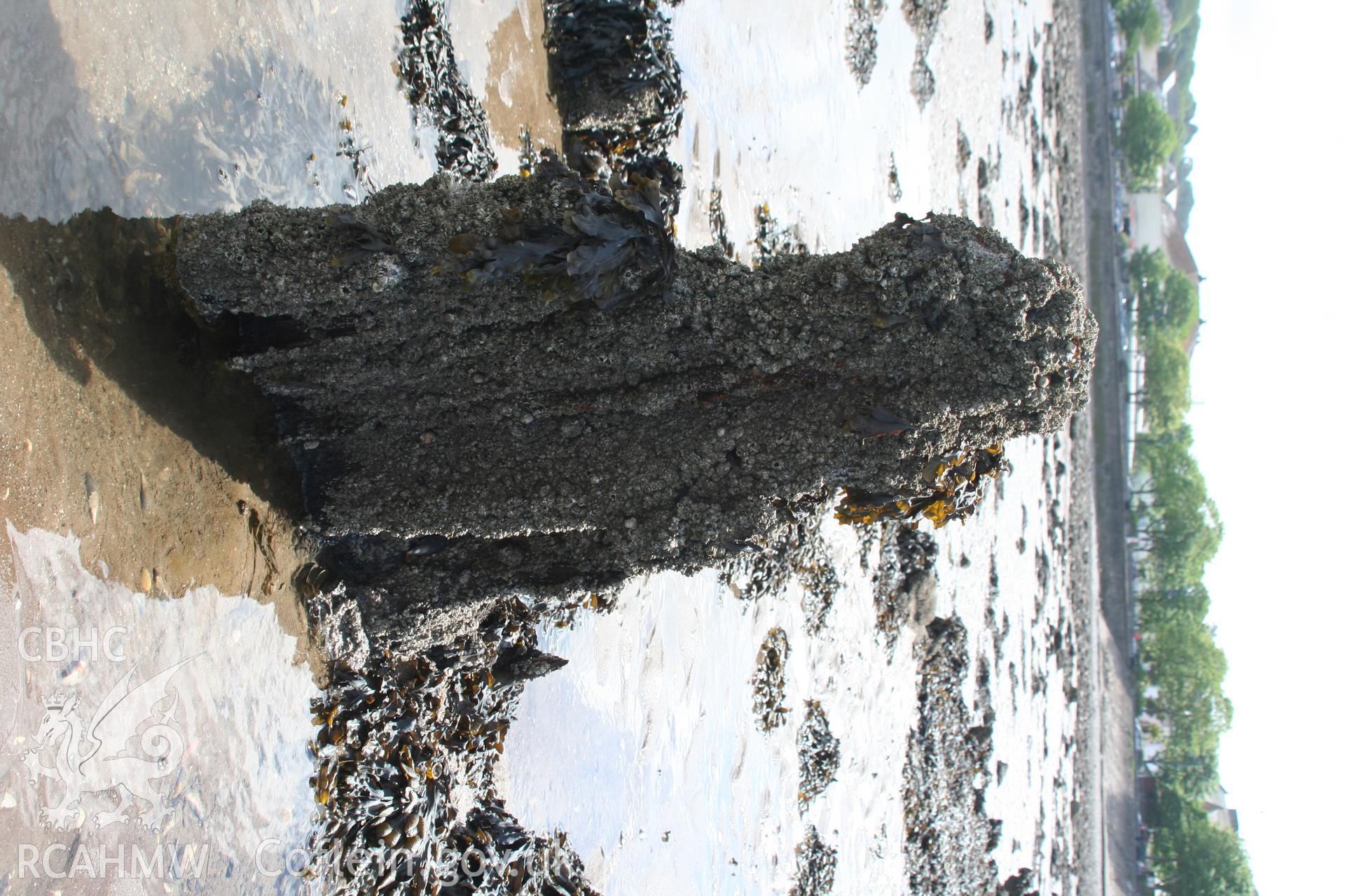 Wreck looking west. In foreground, close up of the remains of the stern post and rudder. In background, remains of the starboard lower frame protruding from the sand.Digital photographs of wreck on the foreshore at the Mumbles, Swansea