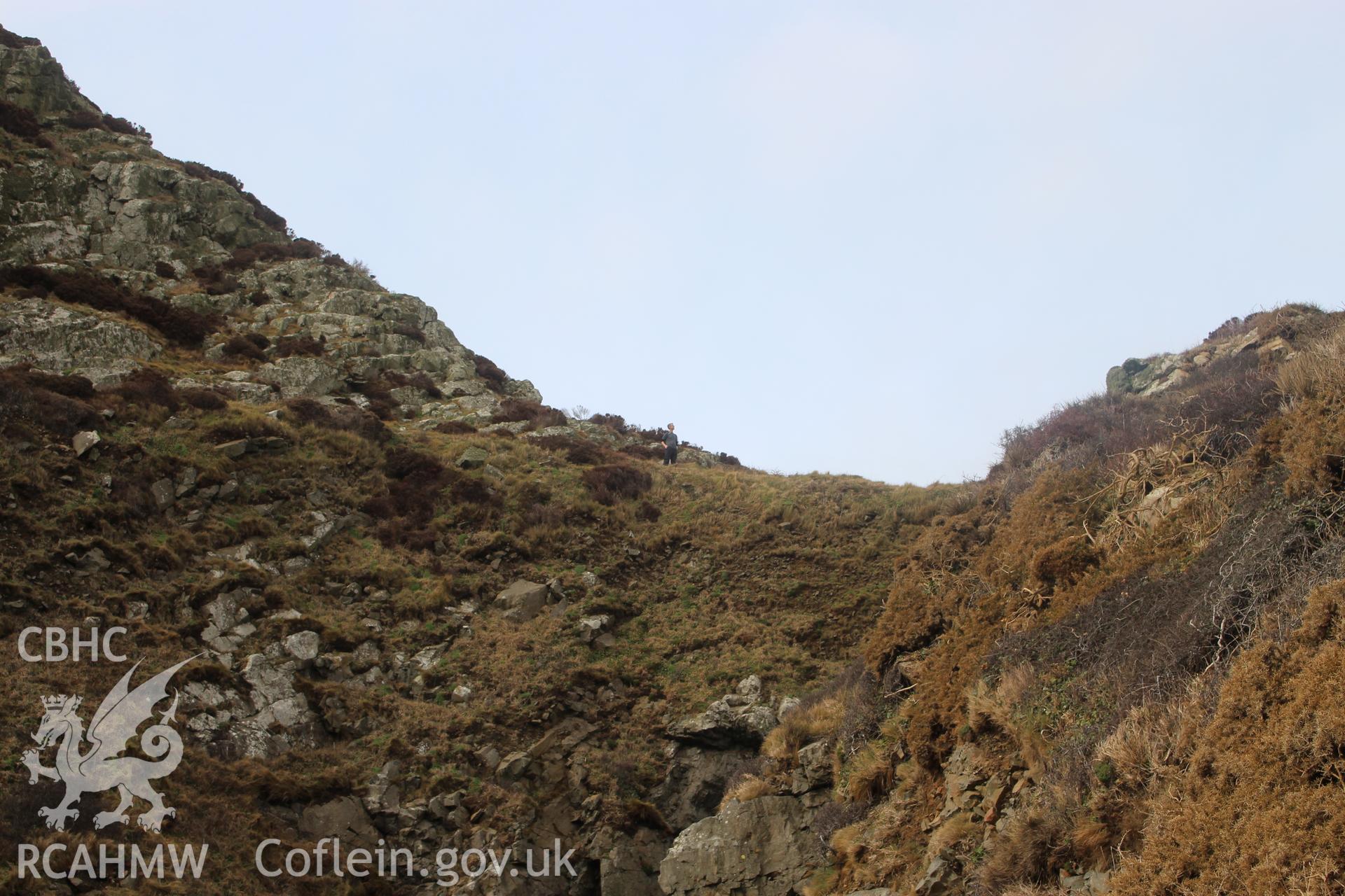 PHOTO SURVEY OF DINAS MAWR, LLANWNDA, PROMONTORY FORT, VIEW OF EROSION ON PROMONTORY NECK FROM SOUTH, WITH FIGURE FOR SCALE