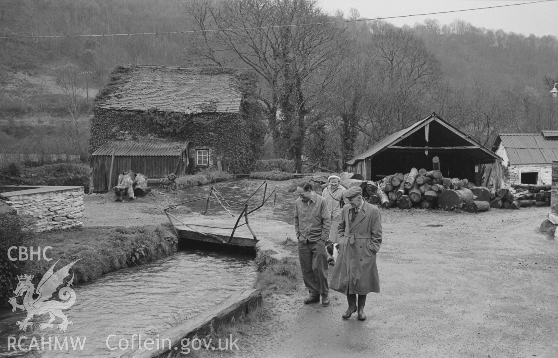 Black and White photograph showing view looking down the mill stream to the mill building (left), with figures in front, at Melin Ceri, Cwmcoy. Photographed by Arthur Chater in April 1962, from Grid Reference SN 300 424, looking south.