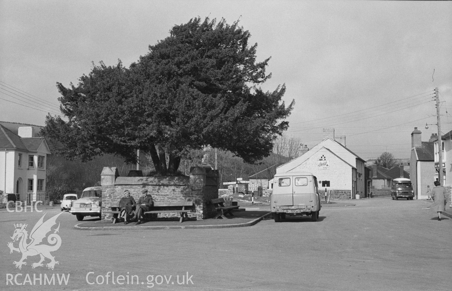 Black and White photograph showing the main square with yew tree at Llangeitho village. Photographed by Arthur Chater in April 1963 from Grid Reference SN 619 597, looking north east.