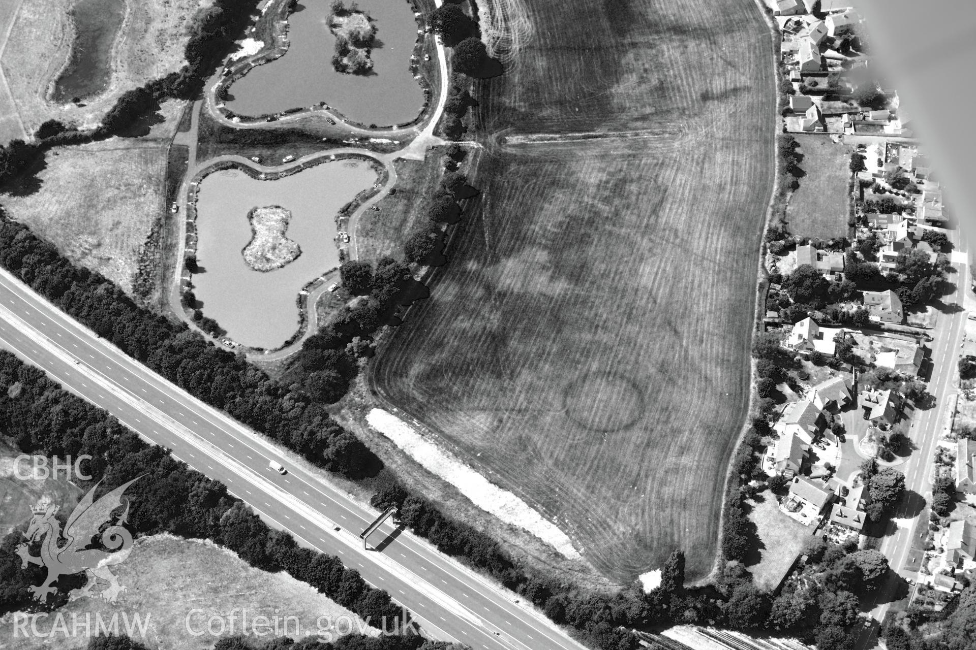 Round barrow cropmarks and the village of Newton Green,south west of Chepstow, with the M48 passing to the south. Oblique aerial photograph taken during the Royal Commission?s programme of archaeological aerial reconnaissance by Toby Driver on 1st August