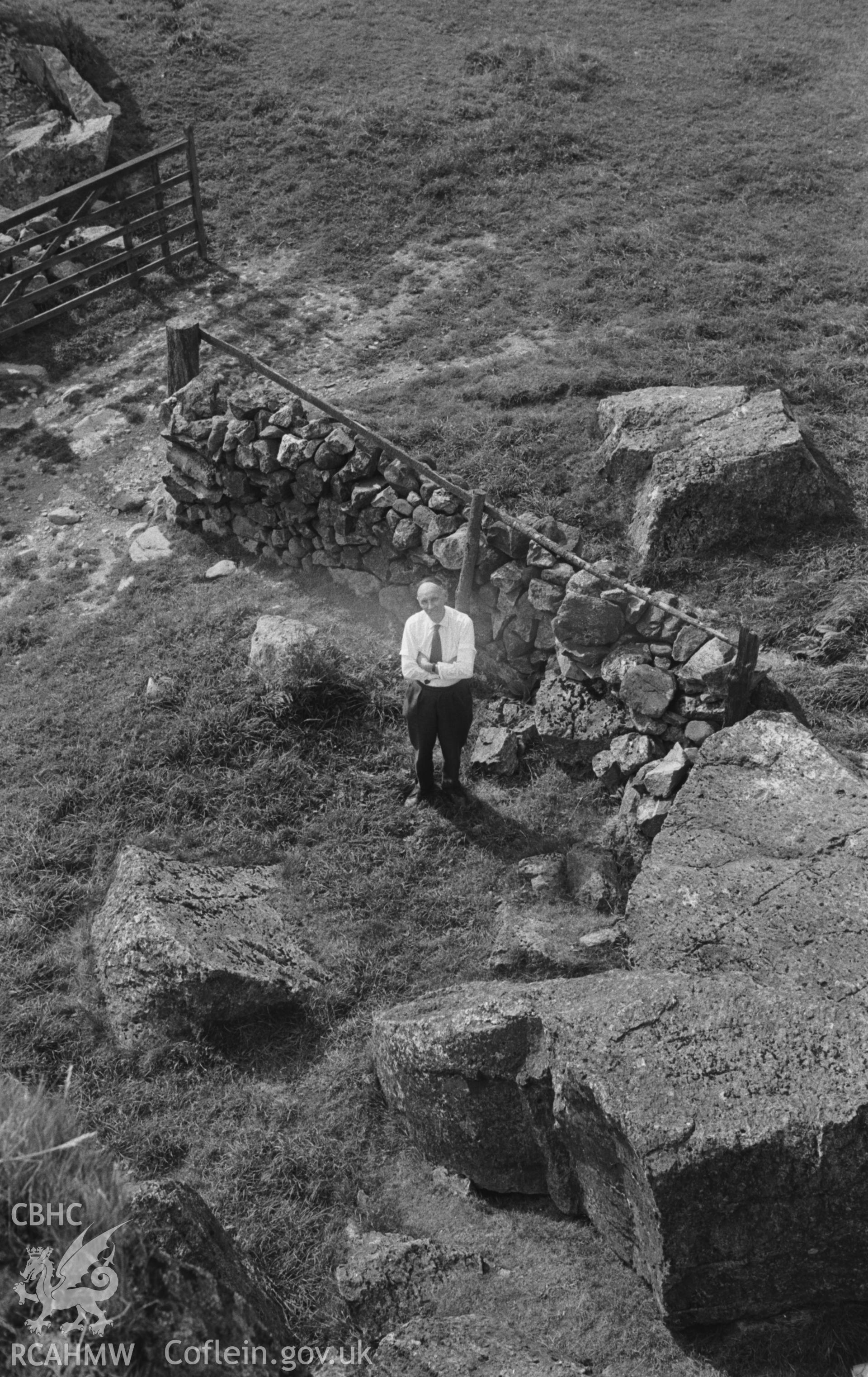 Digital copy of a black and white negative showing man near stone field boundaries at Llanrhaeadr-ym-Mochnant. Photographed by Arthur O. Chater in September 1964.