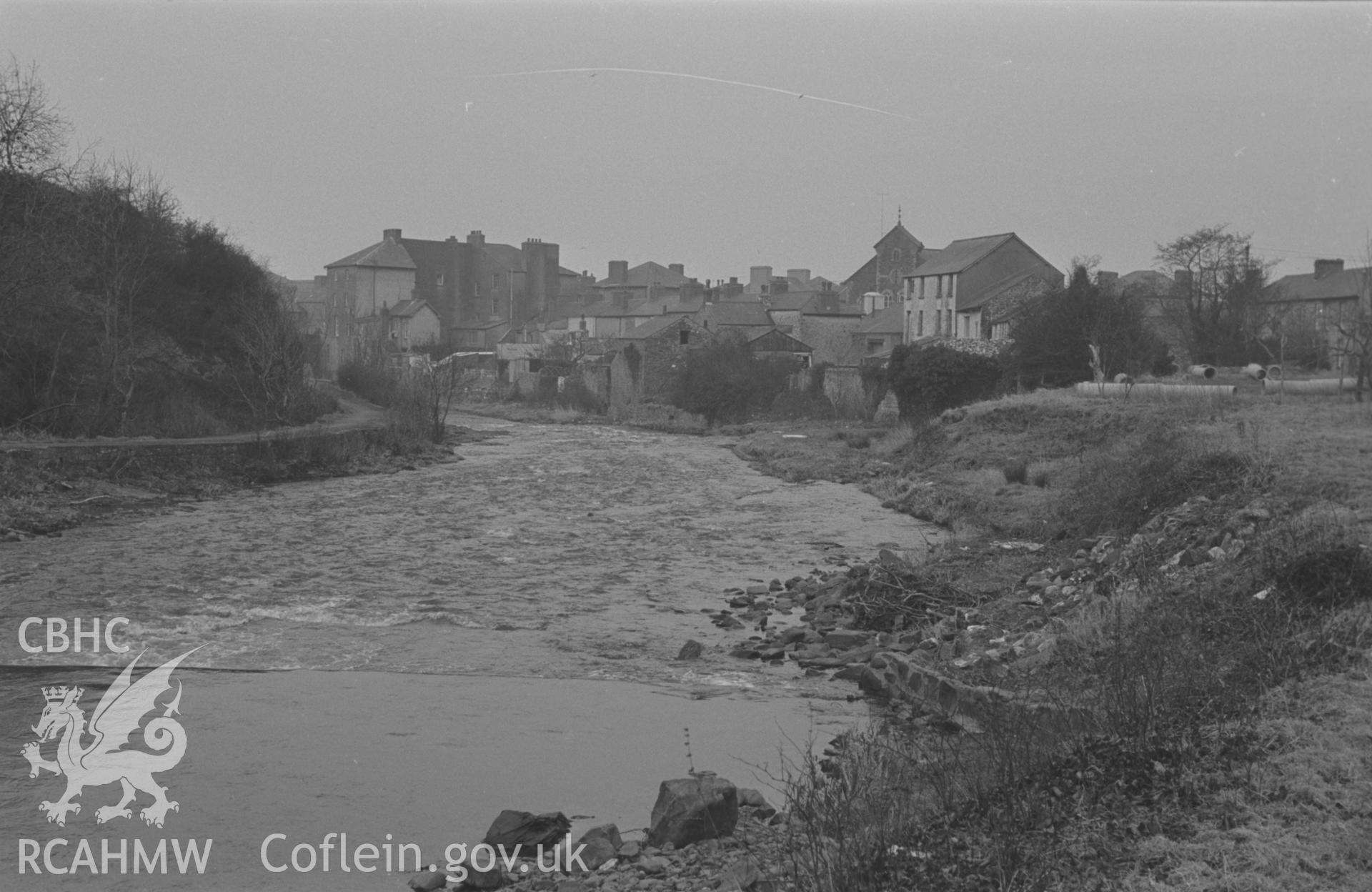 Black and White photograph showing Aberaeron. 'View down the Aeron from the weir just below Lover's Bridge. Chalybeate Well in bushes on the right.' Photographed by Arthur Chater, February 1963. Taken from grid ref: SN 4580 6260, looking north.