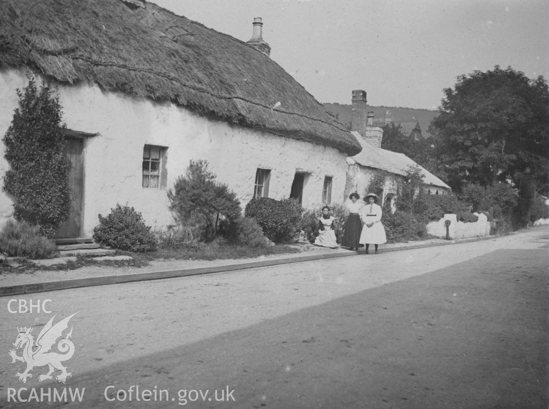 "1910 mud cottages Llangawsai Aberystwyth". Photo of three figures at the roadside. Digitised from a photograph album showing views of Aberystwyth and District, produced by David John Saer, school teacher of Aberystwyth. Loaned for copying by Dr Alan Chamberlain.