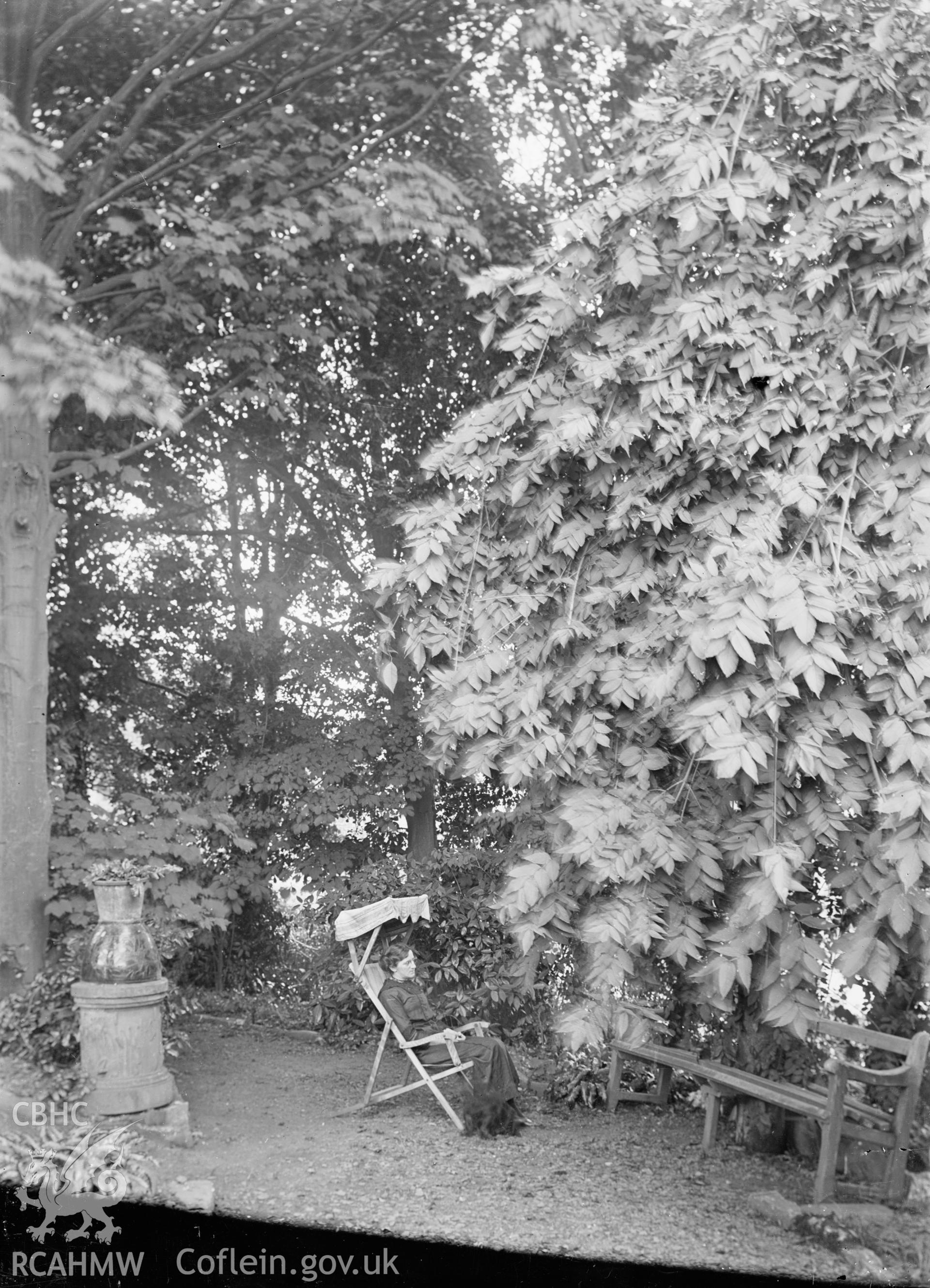 Black and white glass negative showing figure sitting in unknown garden, from National Buildings Record.