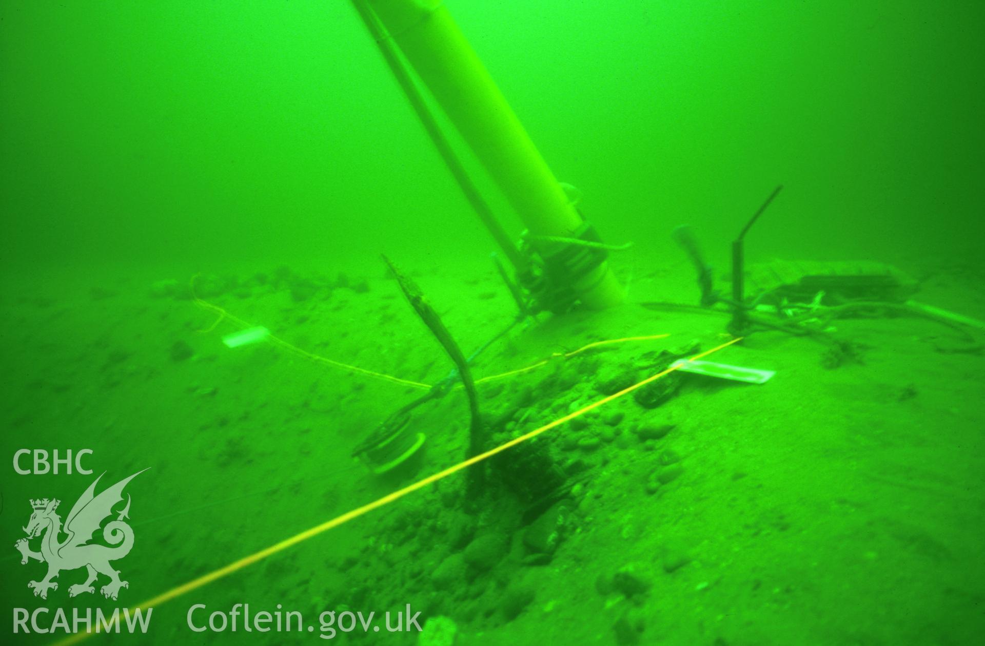 Colour slide. Airlift preparing to excavate wooden cladding from the former location of the submarine, with the straps formerly fastening the cladding to the side of the submarine protruding above the seabed.