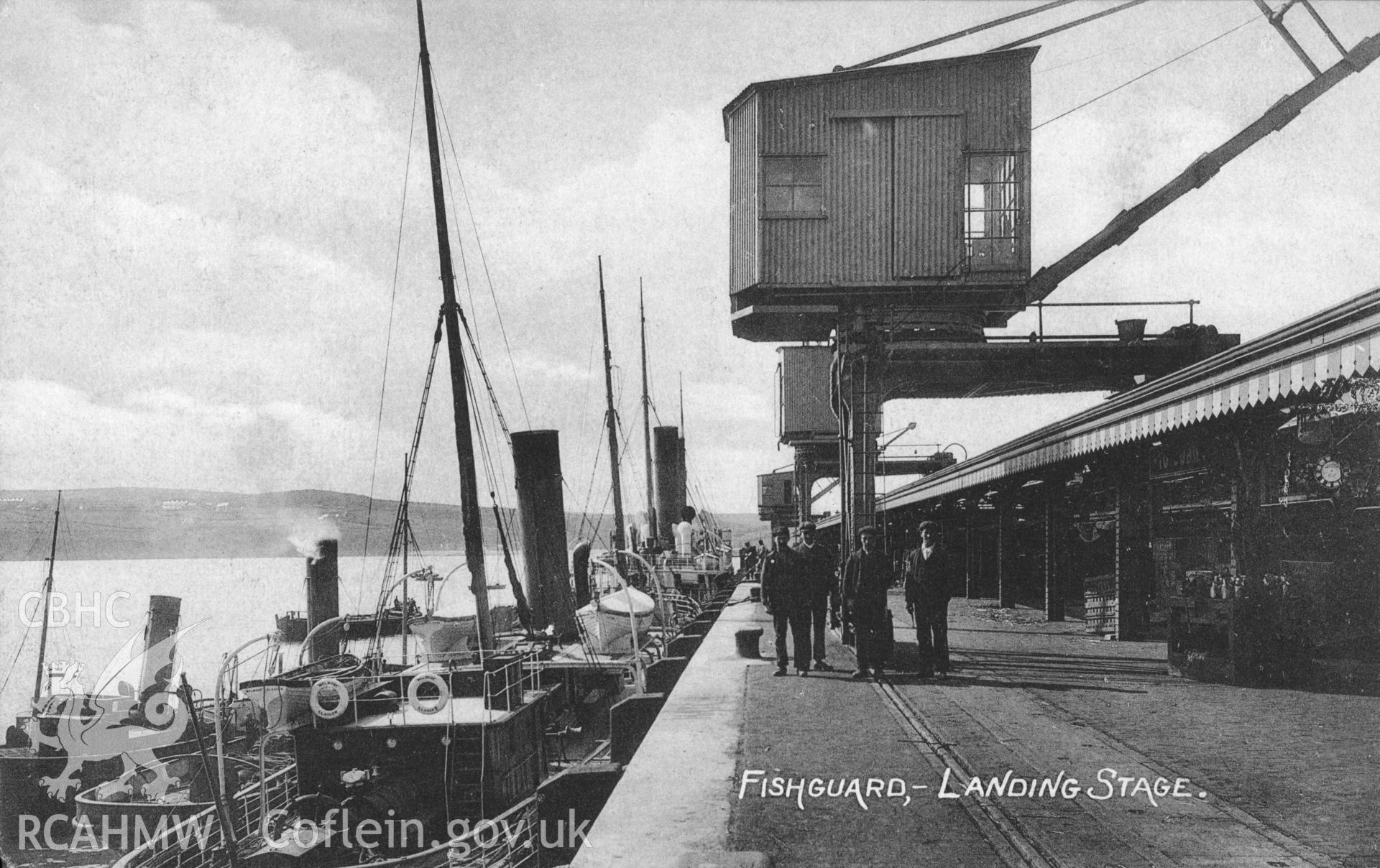 Fishguard Harbour; black and white picture postcard, postmark December 1908(9), showing view of Fishguard Harbour station with loading crane and a variety of smaller craft alongside the quayside.