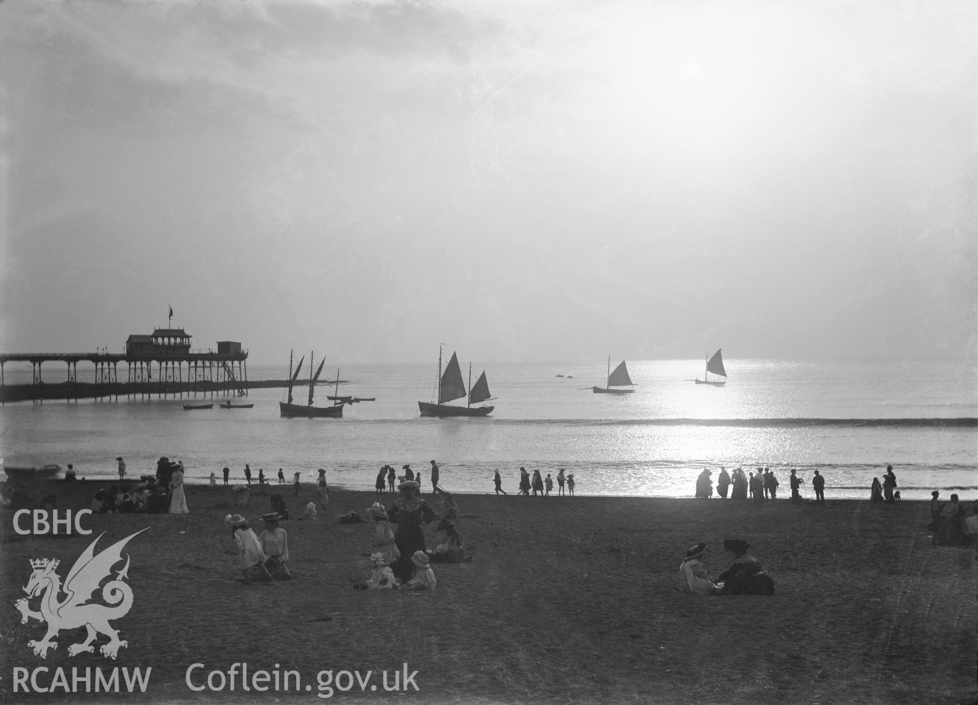 Black and white image dating from c.1910 showing a busy beach scene at Aberystwyth with the Pier in the background.