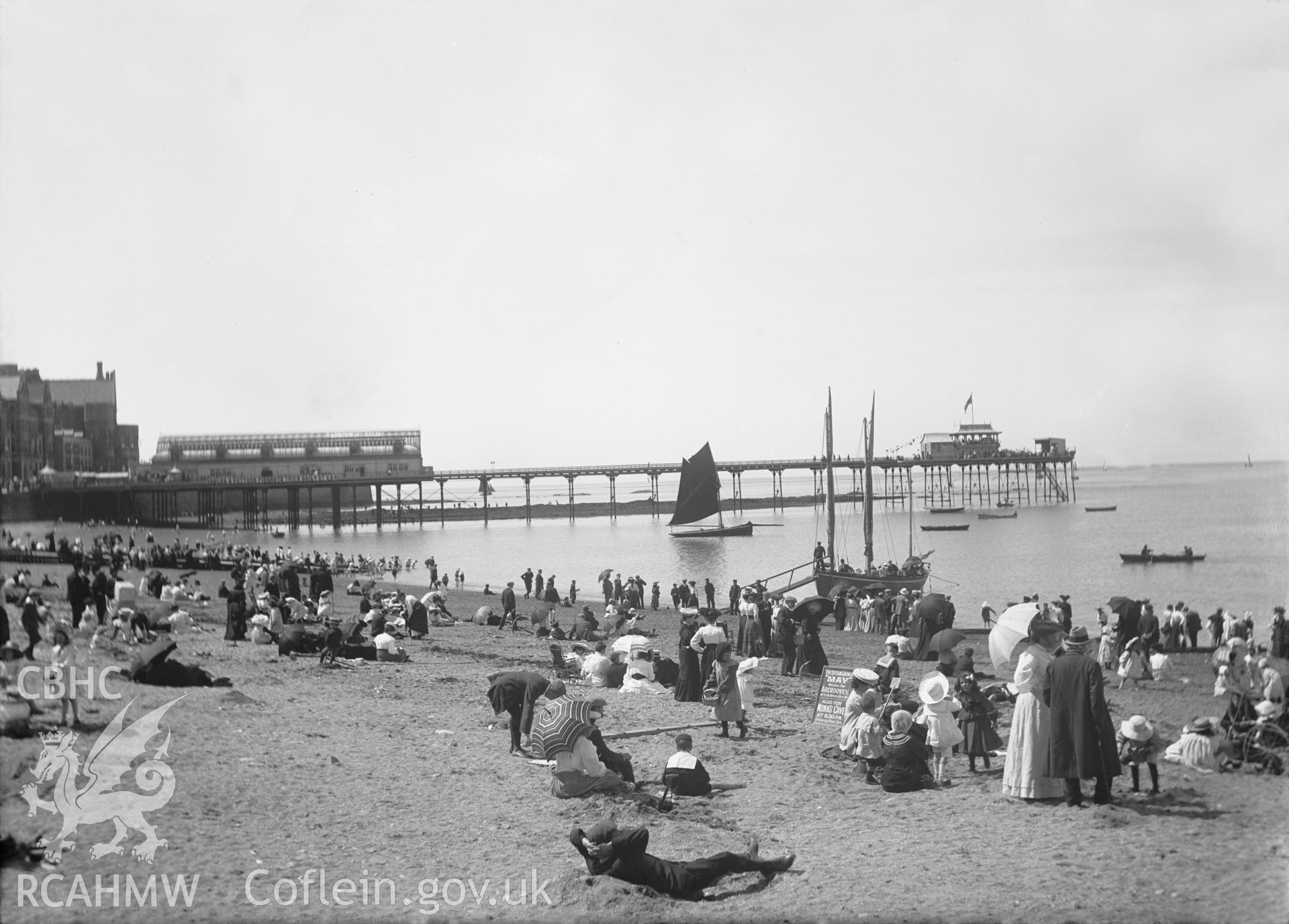 Black and white image dating from c.1910 showing the a busy beach scene at Aberystwyth with the Pier in the background.