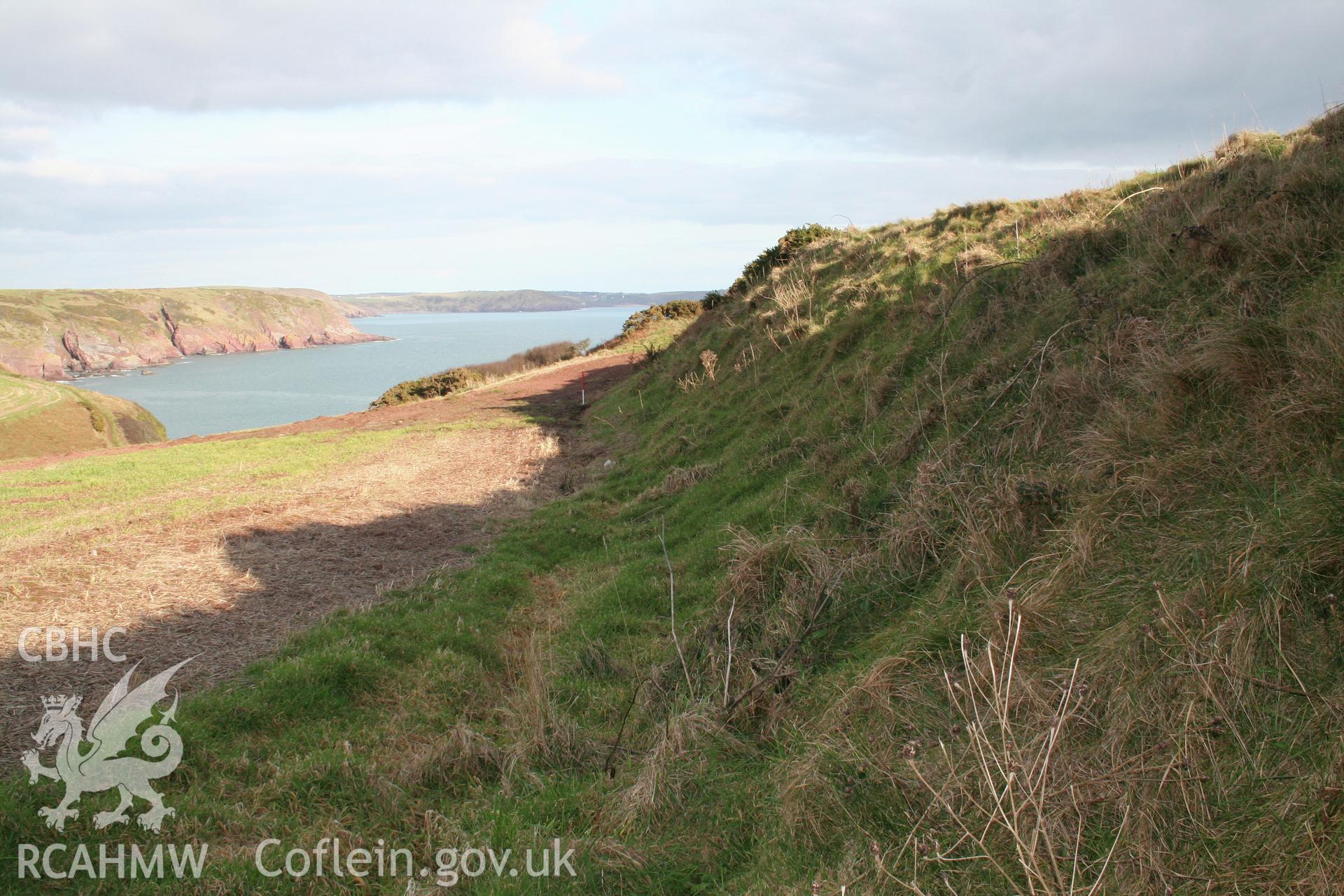 Looking east along the external face of the outer rampart bank of the annexe defences, to the main fort entrance, at scale pole.