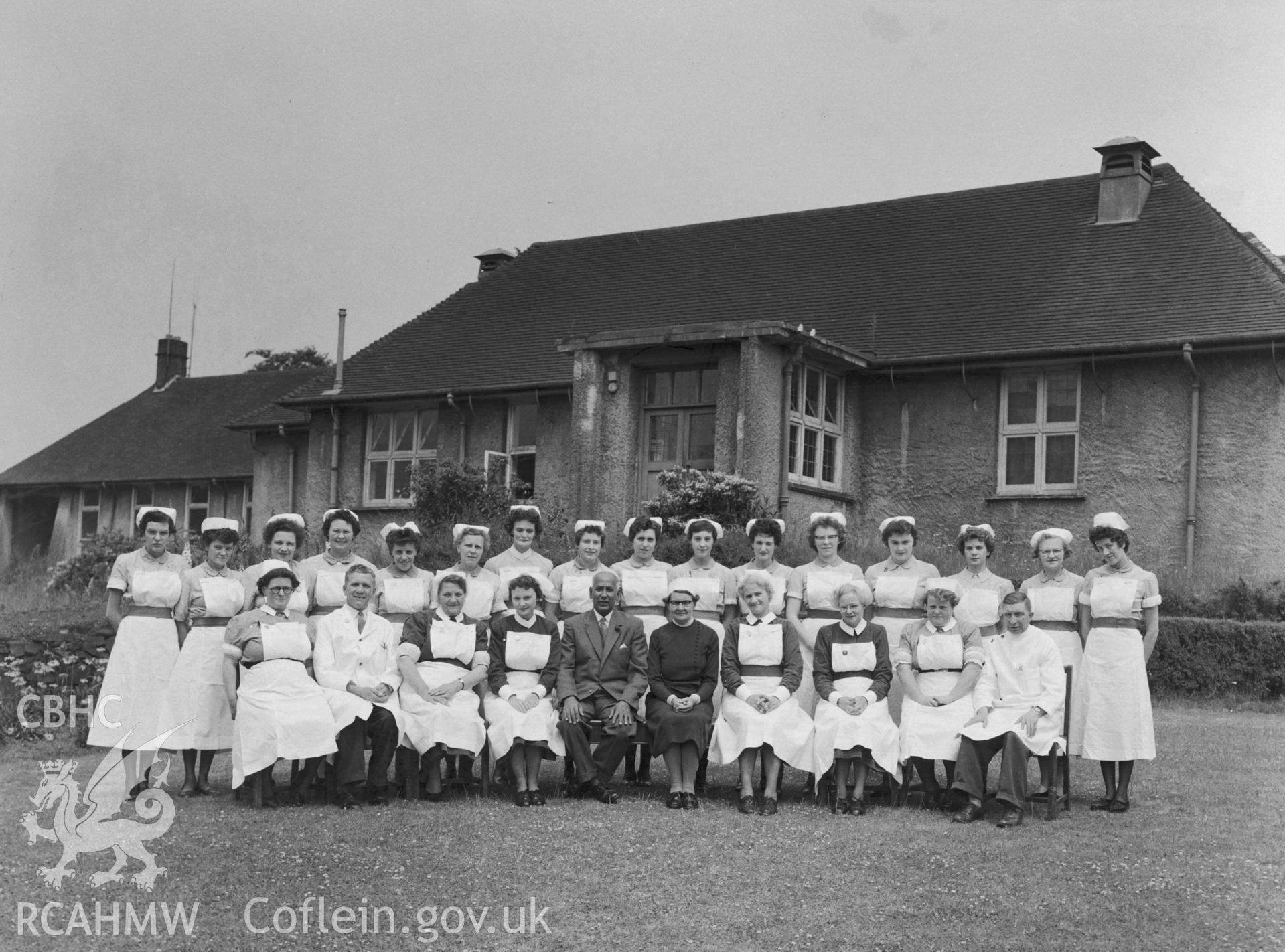 Black and white photograph showing nursing staff outside Abertillery Hospital. Staff are identified as (rear) N. Rogers, N. Collins, N. Purnell, N. Hinder, N. Nash, N. Jenkins, N.R. Jones, N. Janes, N. Haycock, N.H. Jones, N. Bowditch, N.Judge, N. Price, N. Szabo, N. Priddy, N. Perry (front) S.N. Meredith, Mr Aubrey, S. Morgan, S. Prosser, Mr R.W. Scanlon, Matron G.E. Body, S. Lewis, S. Poultney, S.N. Hopkins, and Mr Cleaton.