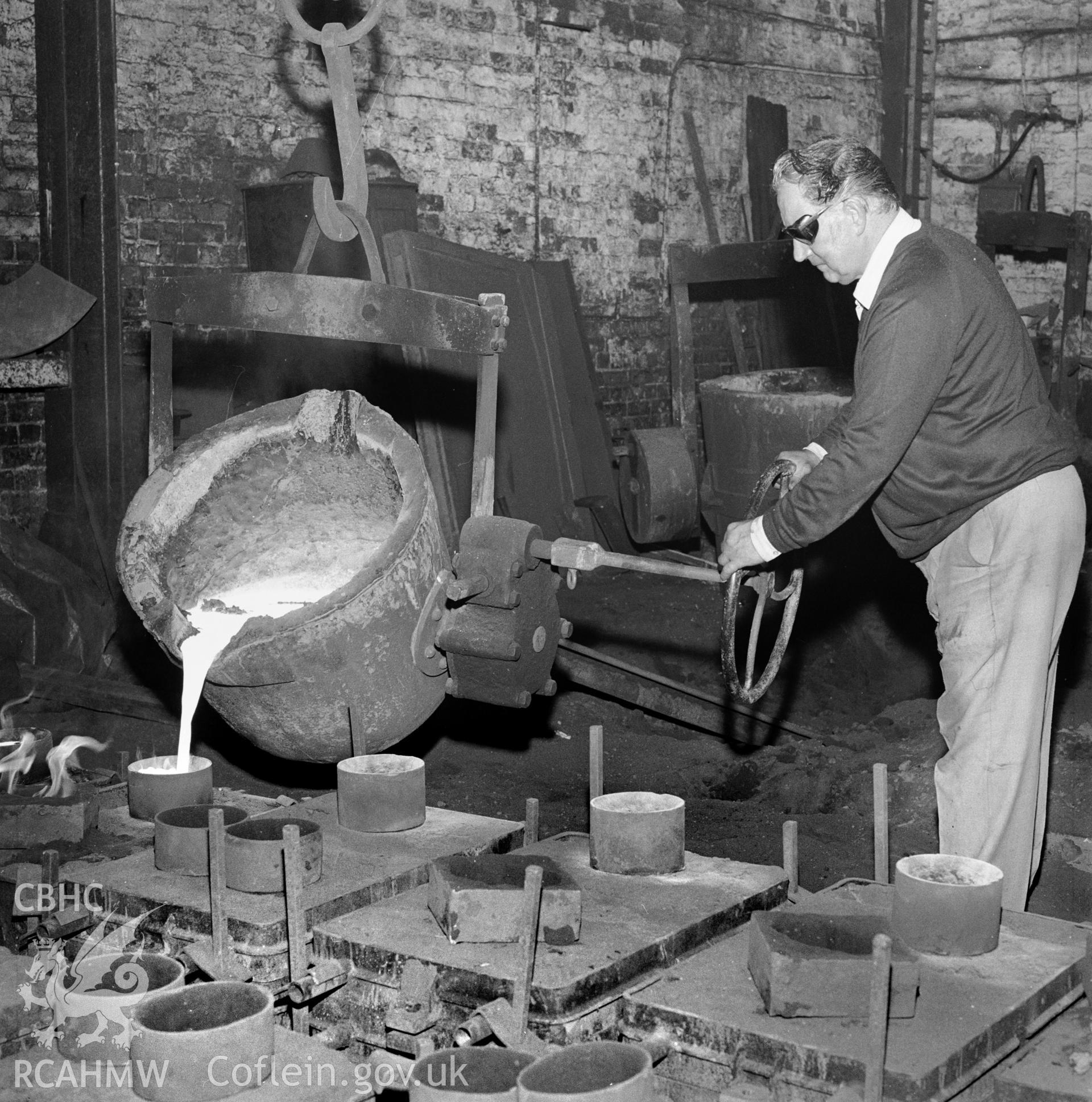 The ladle, moved by crane (gantry) is being tilted, and the molten iron poured into mould boxes