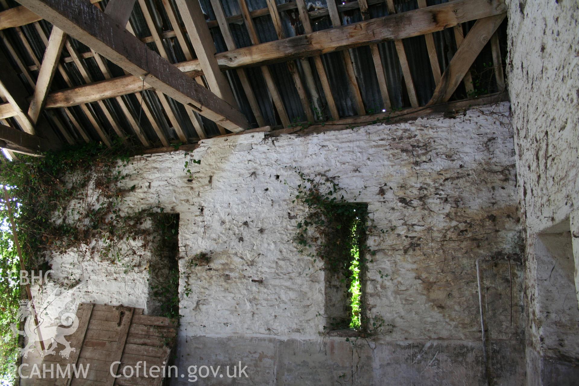 Interior of framed barn, showing later threshing-bay doorway partly blocked in stone.