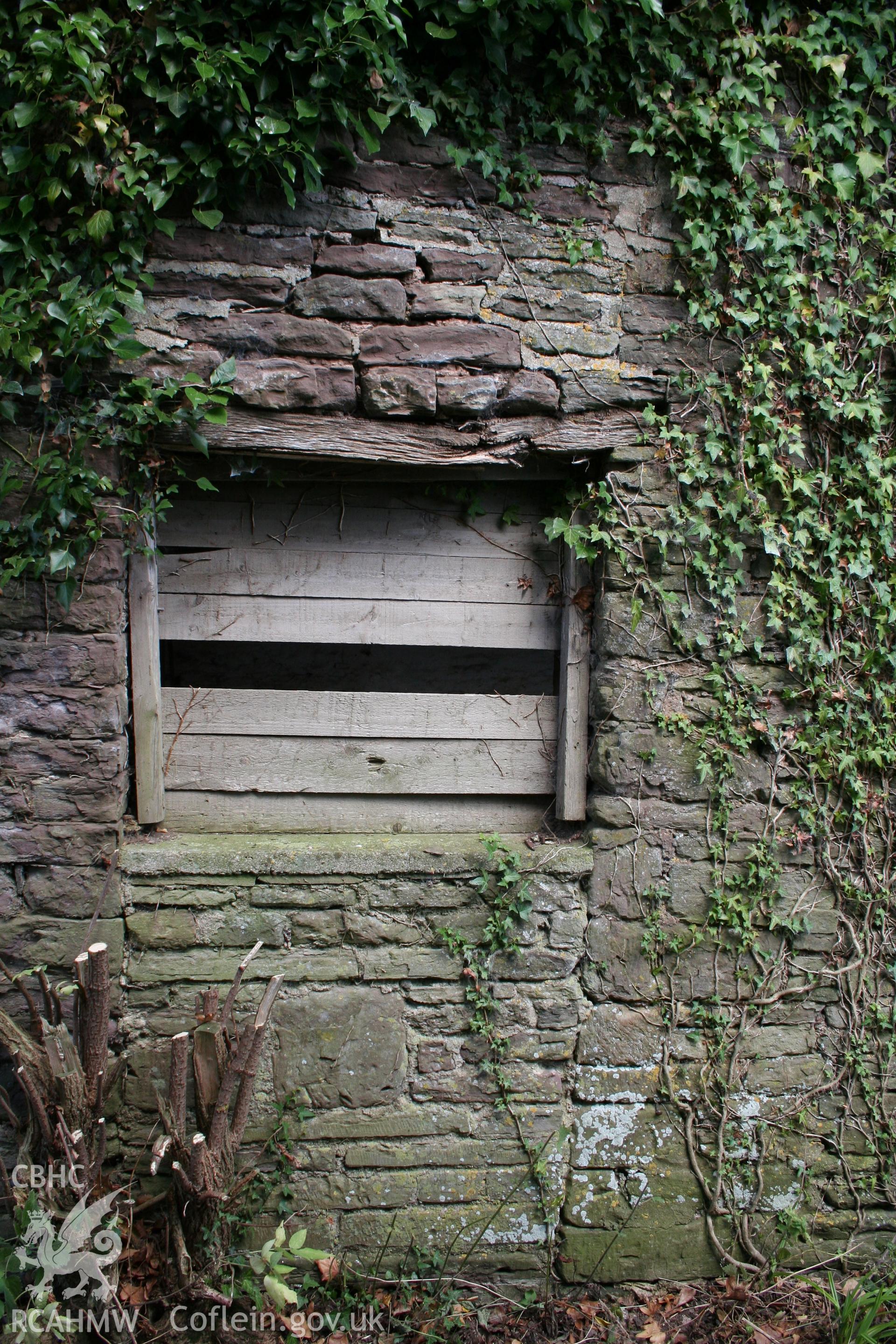 Exterior of south-west elevation of cowhouse/stable, showing a former doorway, now a window.