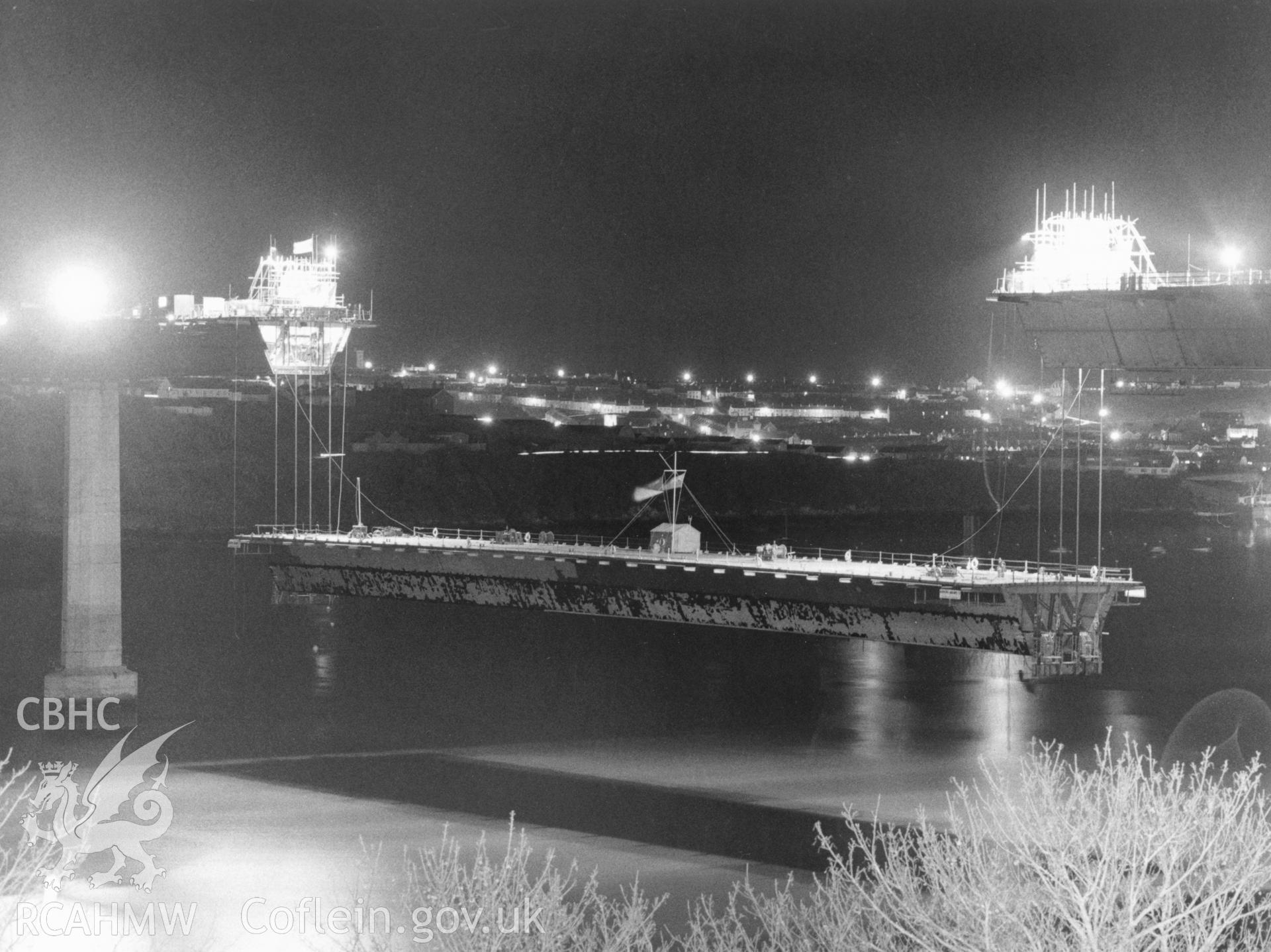 1 b/w print showing central section of Cleddau Bridge, Milford Haven, being lifted into place (at night), collated by the former Central Office of Information.