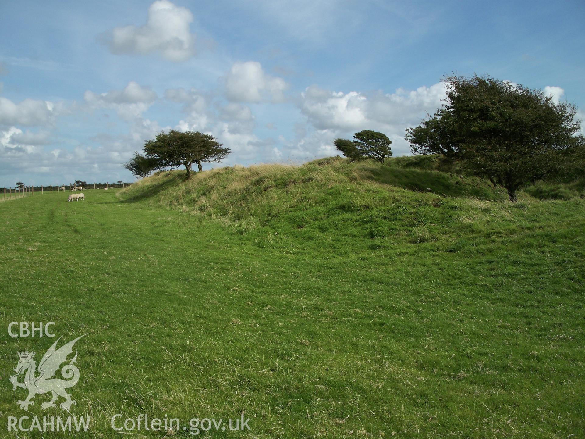 Looking east along the extant outer rampart bank defining the north side of the enclosure. A later quarry pit cuts into the bank on the right hand side of the view.