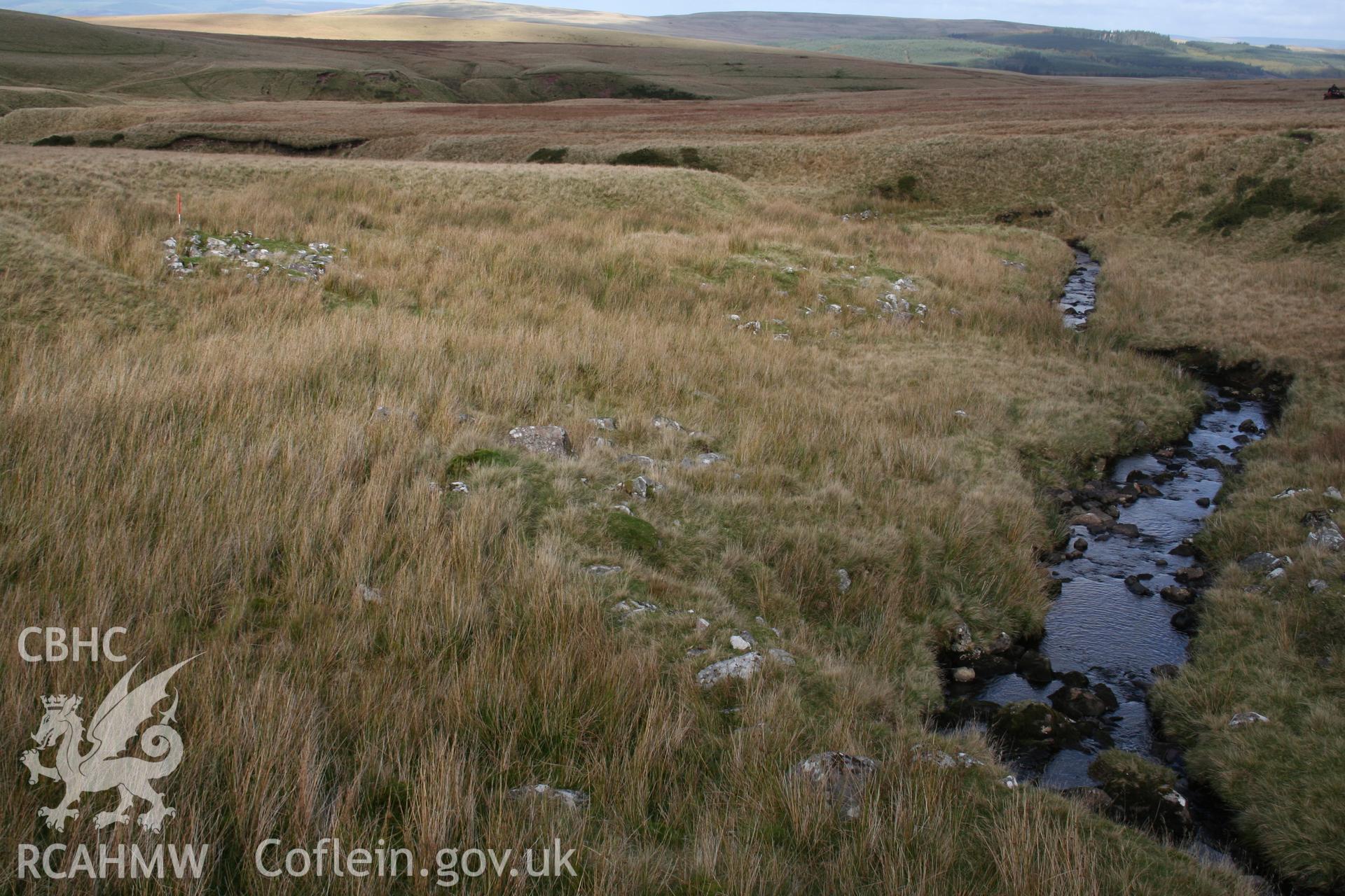 Settlement remains along the cutting of the upper Usk, showing as grey spreads of stone, seen from the north.