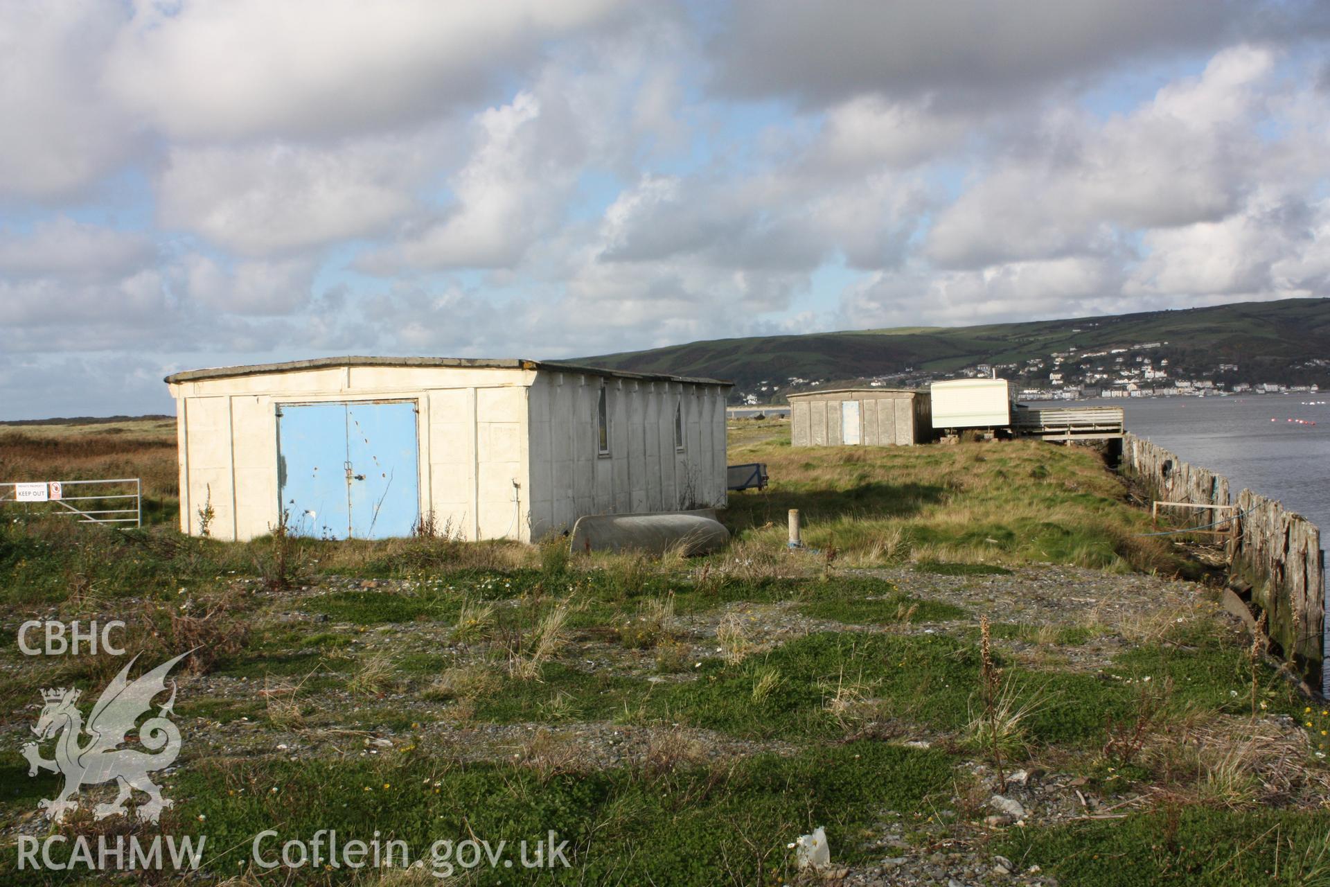Hut (in background) with associated mobile home and exterior decked-area spanning the degraded wharf front.