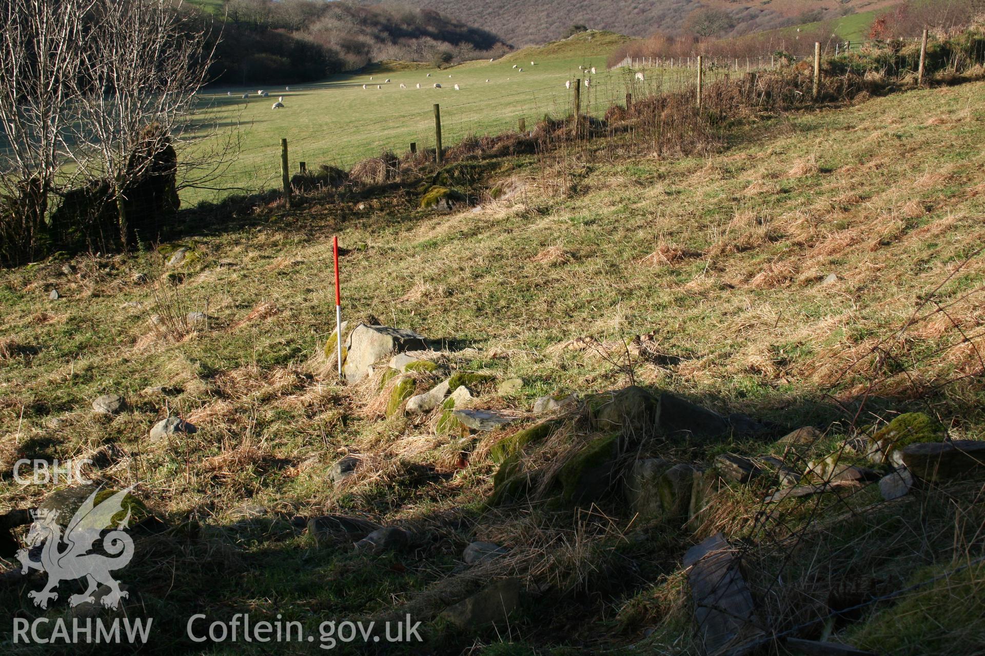 Traces of end of north wall, 1m scale; undulations in field beyond mark site of medieval precursor (NPRN 418086).