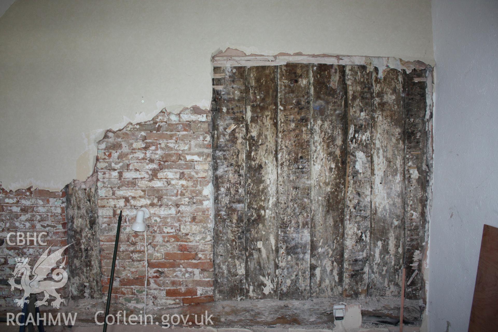 Internal; Living room, former service room, showing rear of post-and-panel partition and 17th centruy brick blocking.