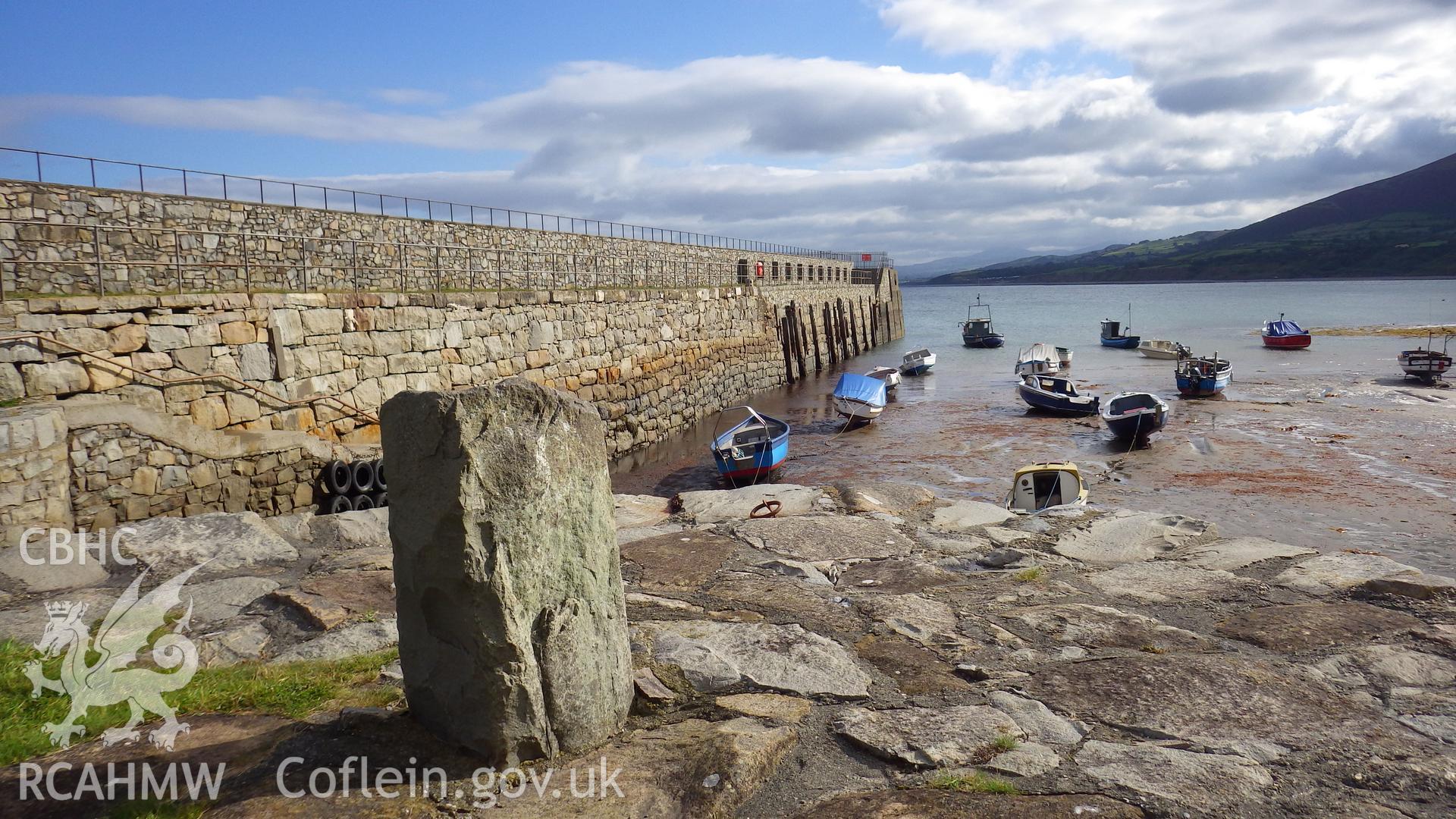Inner wall of the harbour breakwater with large stone mooring bollard at entrance to small dock in foreground
