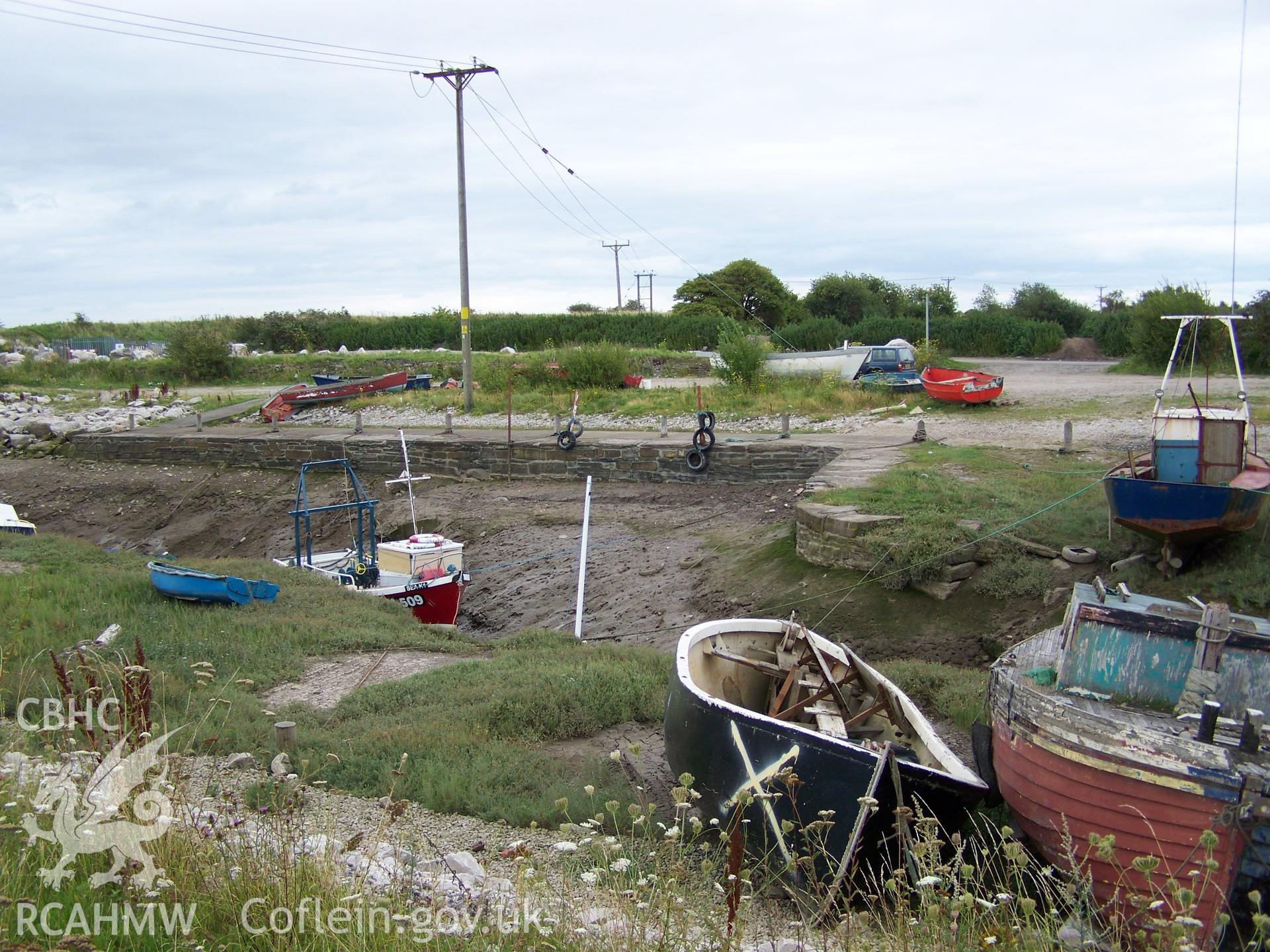 Facing wall of eastern quay and sluice entance to the right behind derelict small craft in foreground