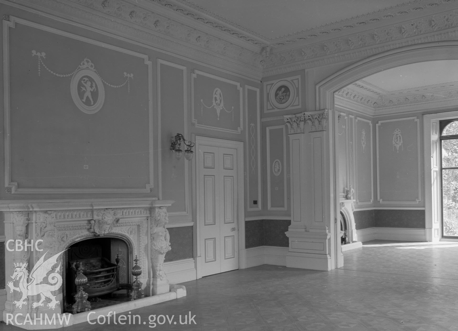A view of an ornate room with a carved marble fireplace. The room is divided in two by a large arch