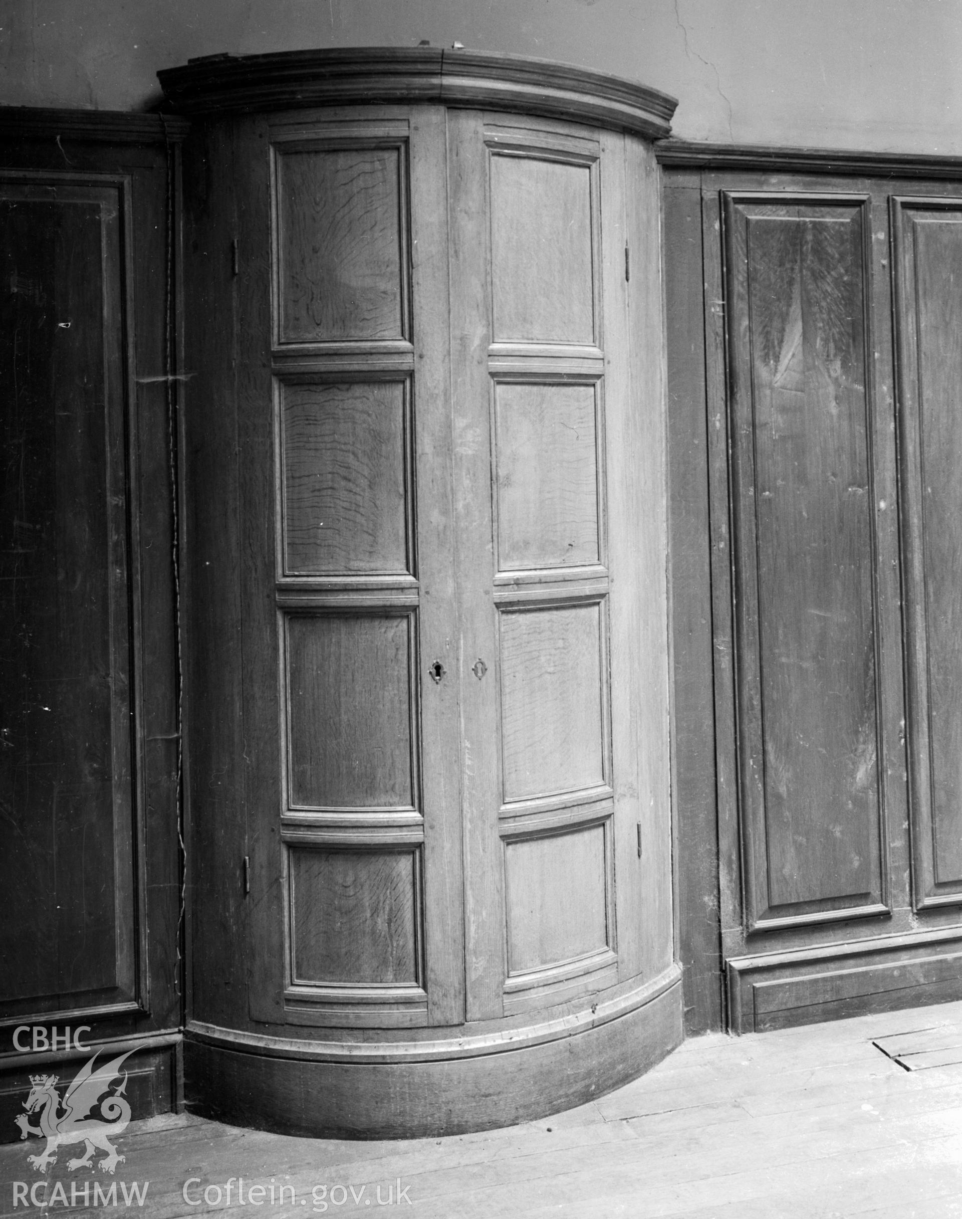 A wooden bow fronted cupboard, incorporated in the wood panelling of the walls.