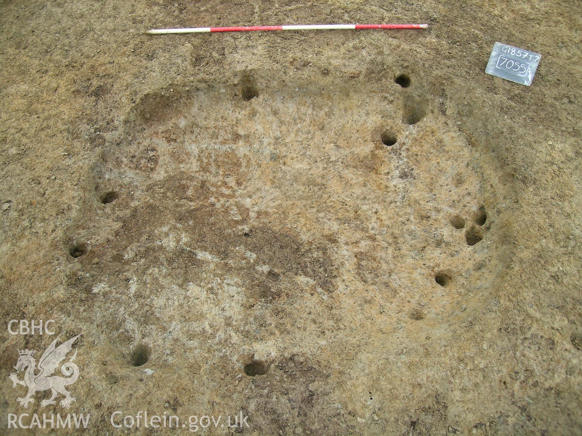 Digital photograph from excavation of Parc Bryn Cegin, Llandygai, by Gwynedd Archaeological Trust. [7055] vertical shot, from NE (numbers refer to context records). Scale 1x2m.
