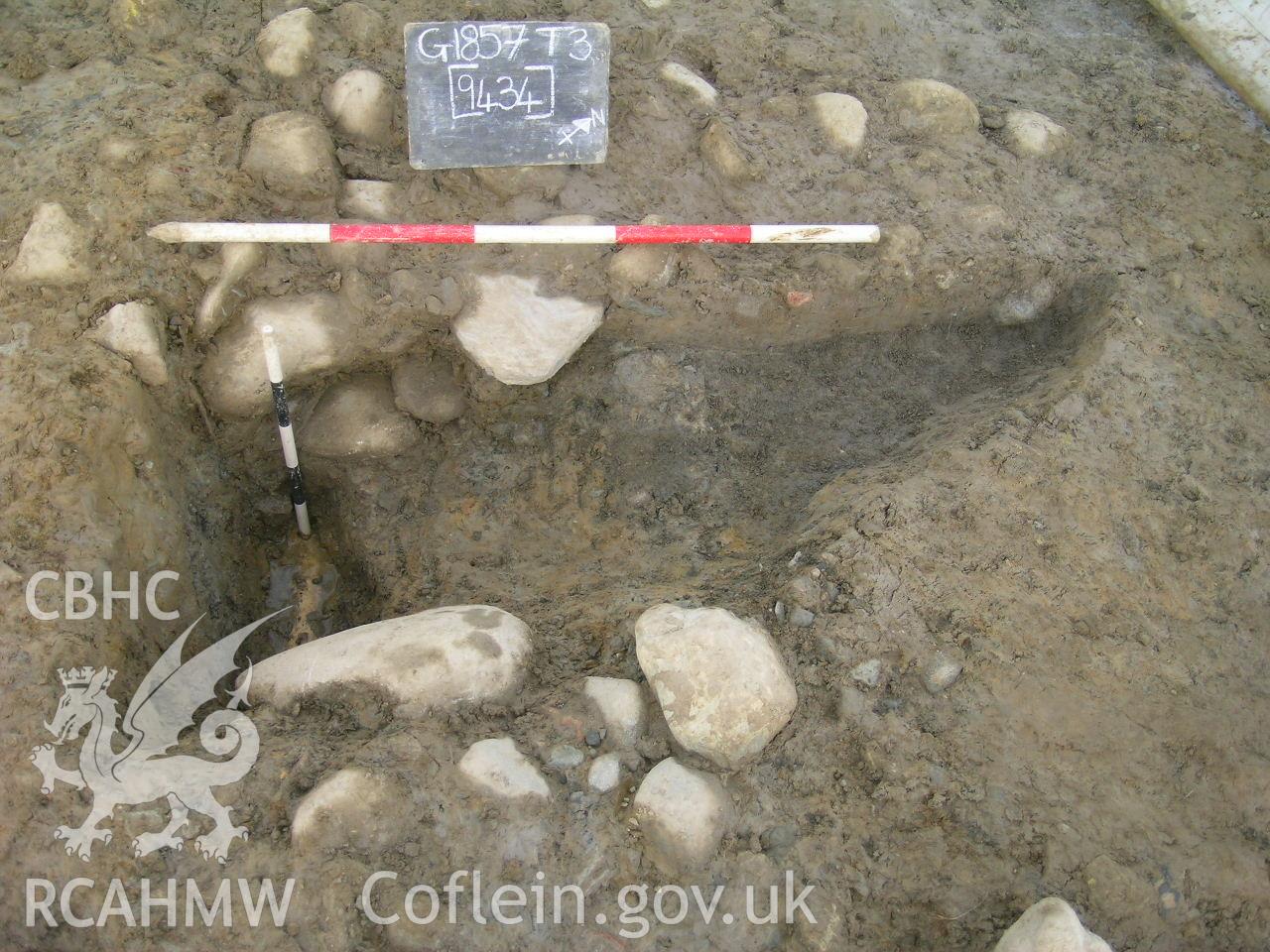 Digital photograph from excavation of Parc Bryn Cegin, Llandygai, by Gwynedd Archaeological Trust. Half section of pit [9434] and field drain, from NW (numbers refer to context records). Scale 1x1m, 1x0.5m.