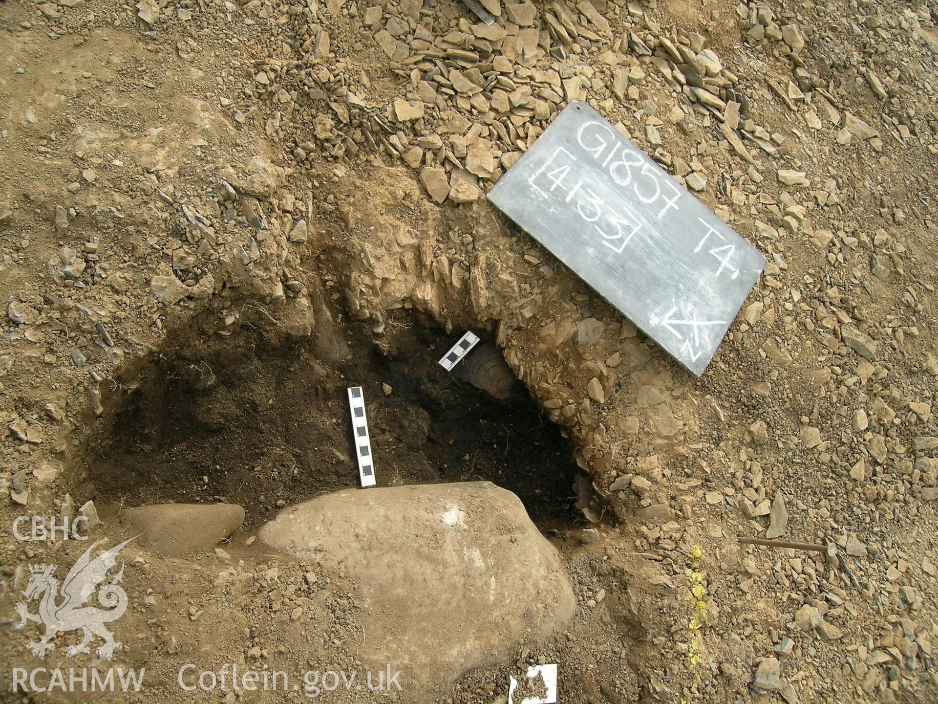 Digital photograph from excavation of Parc Bryn Cegin, Llandygai, by Gwynedd Archaeological Trust. Pot (SF555) & (SF559) in pit [4133] with board, from NNW (numbers refer to context records). Scale 1x0.1m.