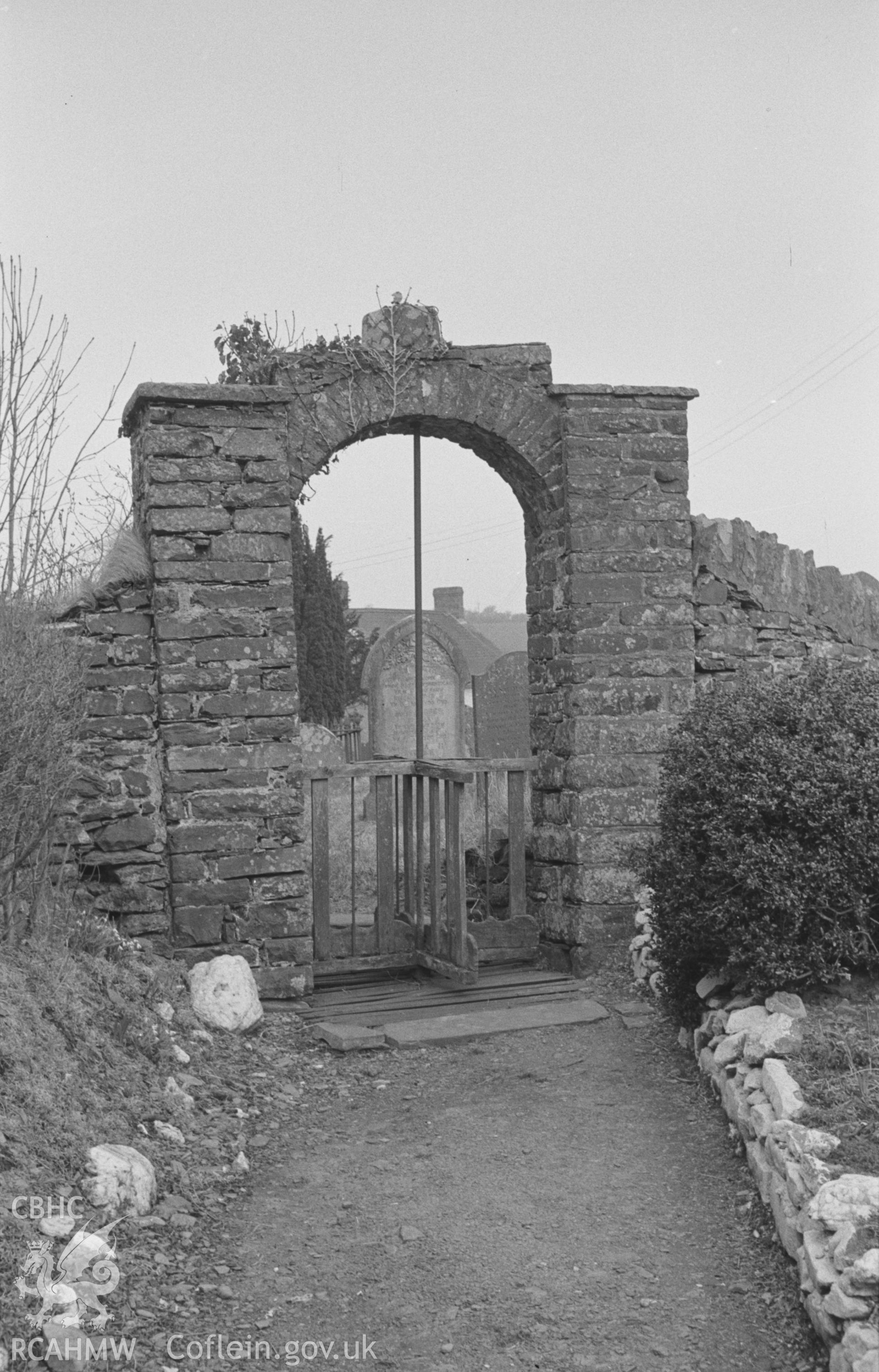 Black and White photograph of south-east gate of churchyard showing stem of Norman Font placed on top, with revolving gate below, Lledrod. Photographed by Arthur Chater in April 1963 at Grid Reference SN 646 702, looking north west.