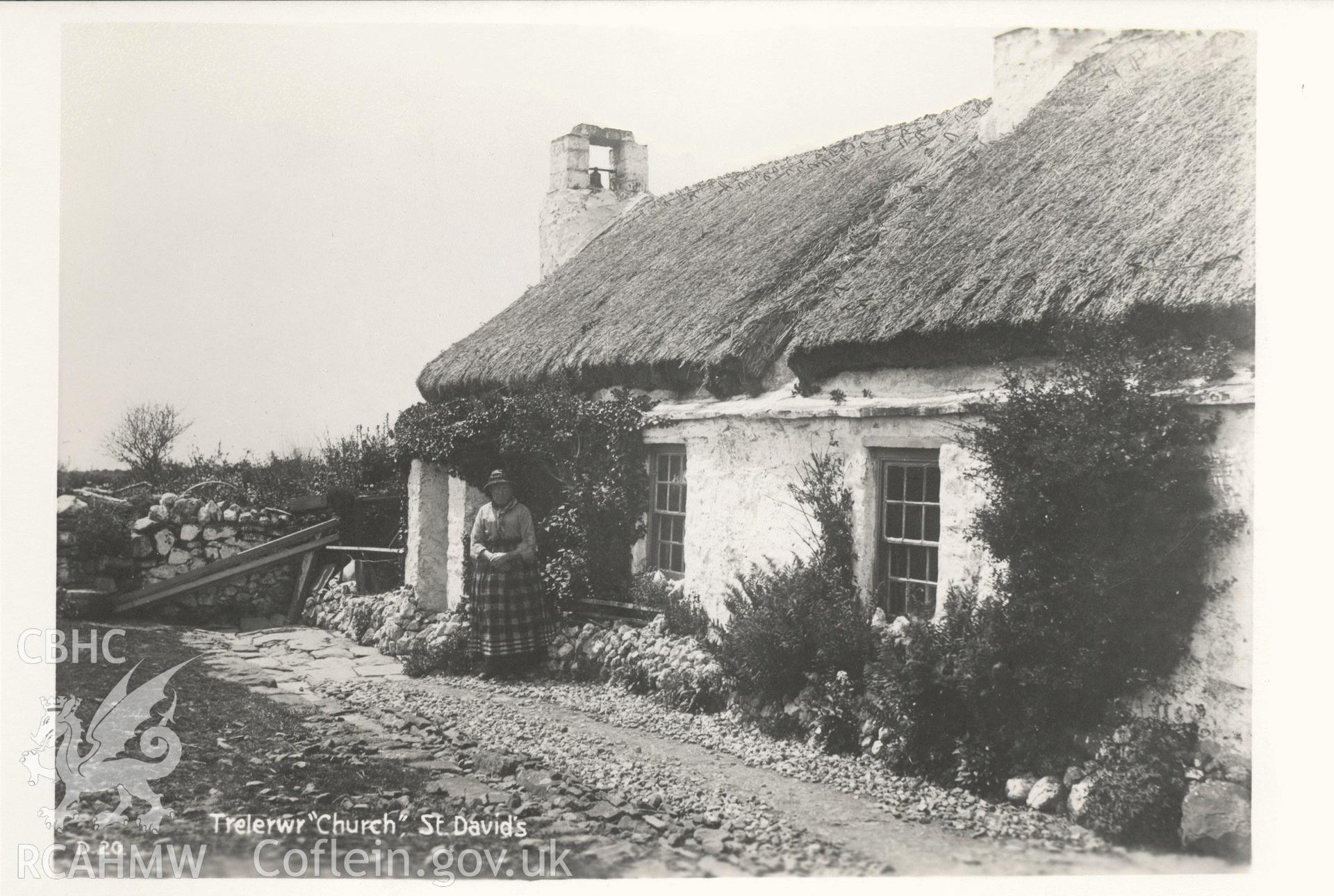 Digitised postcard image of Trelerwr cottage, St David's with figure, W.M. Mendus, Chemists, St David's. Produced by Parks and Gardens Data Services, from an original item in the Peter Davis Collection at Parks and Gardens UK. We hold only web-resolution images of this collection, suitable for viewing on screen and for research purposes only. We do not hold the original images, or publication quality scans.