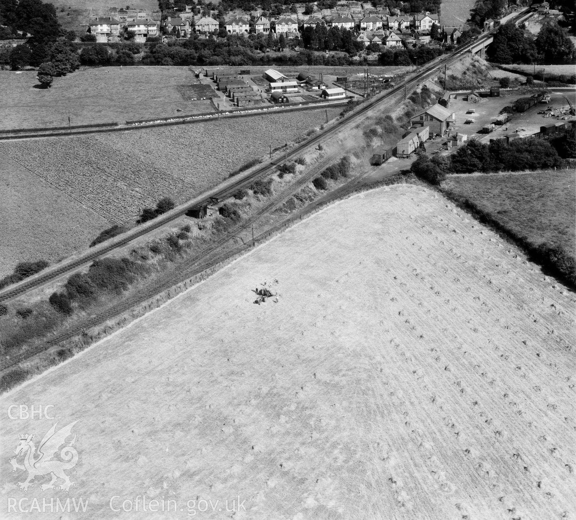 View of Coleford, Monmouth, Usk & Pontypool railway goods yard, north east of Usk, showing men with tractor and haycocks and an unidentified military camp. Oblique aerial photograph, 5?" cut roll film.