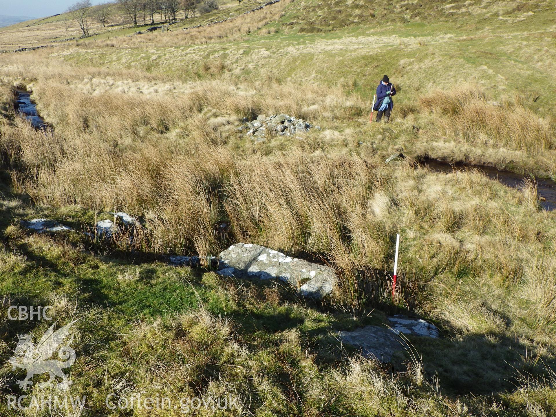The person is standing just behind the bank that forms the sheep wash, just beyond which is stone pile, NPRN 529443, with the horizontal slab in the foreground, looking north.