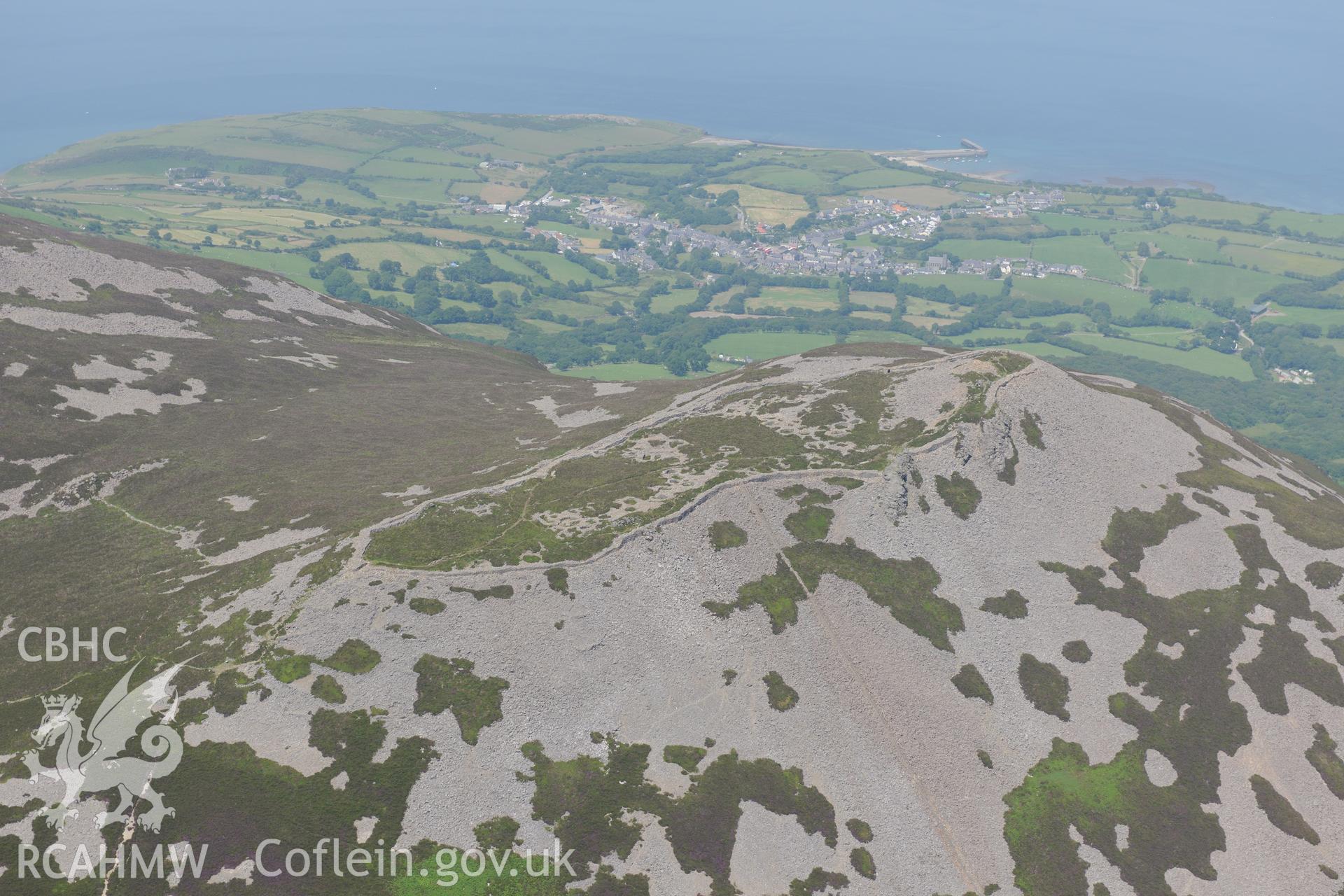 Tre'r Ceiri hillfort with the village of Trefor beyond, on the Lleyn Peninsula. Oblique aerial photograph taken during the Royal Commission?s programme of archaeological aerial reconnaissance by Toby Driver on 12th July 2013.