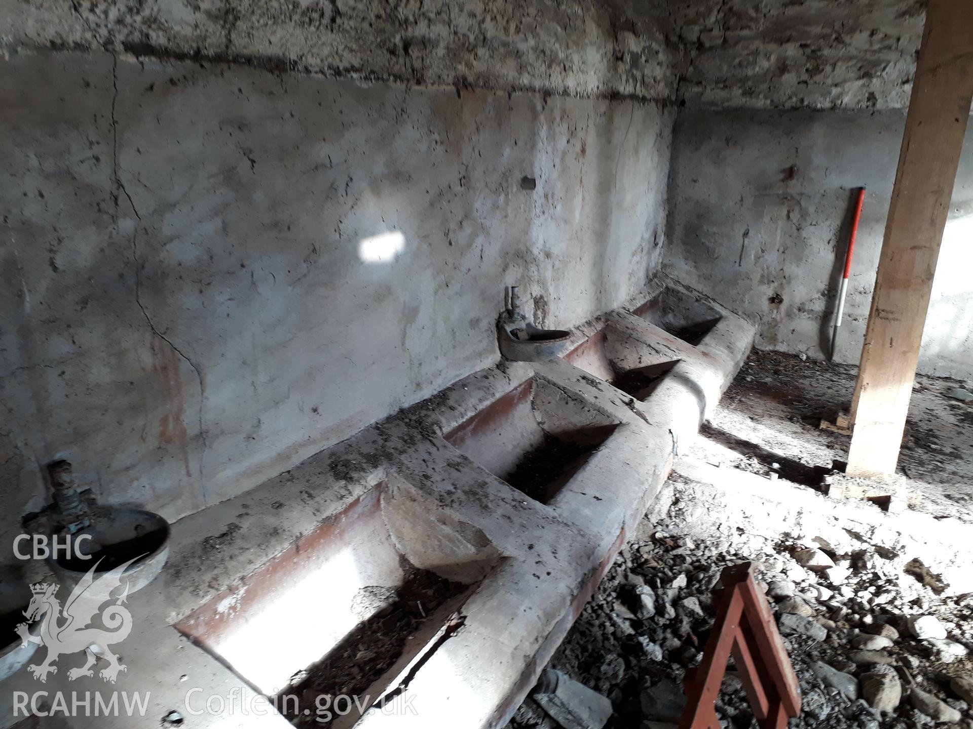 Barn interior view north-east, modern animal troughs. 1m scale. Photographed as part of archaeological building recording conducted at Bryn Ysguboriau, Llanelidan, Denbighshire, carried out by Archaeology Wales, 2018. Project no. P2587.