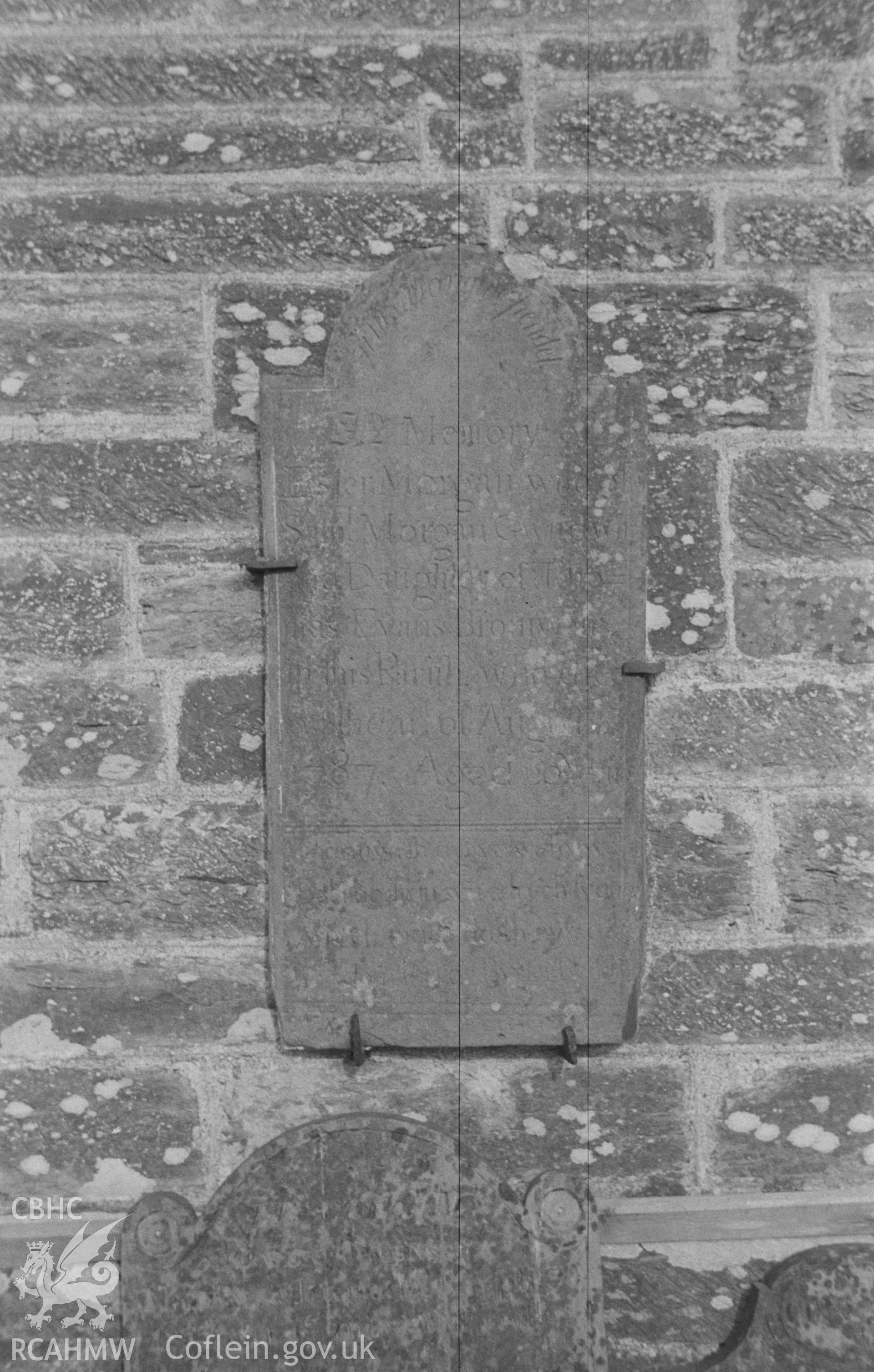 Digital copy of a black and white negative showing tombstone fixed on outer west wall of St Michael's Church, Troedyraur, east of Cardigan. Photographed in April 1963 by Arthur O. Chater from Grid Reference SN 3270 4537, looking east.