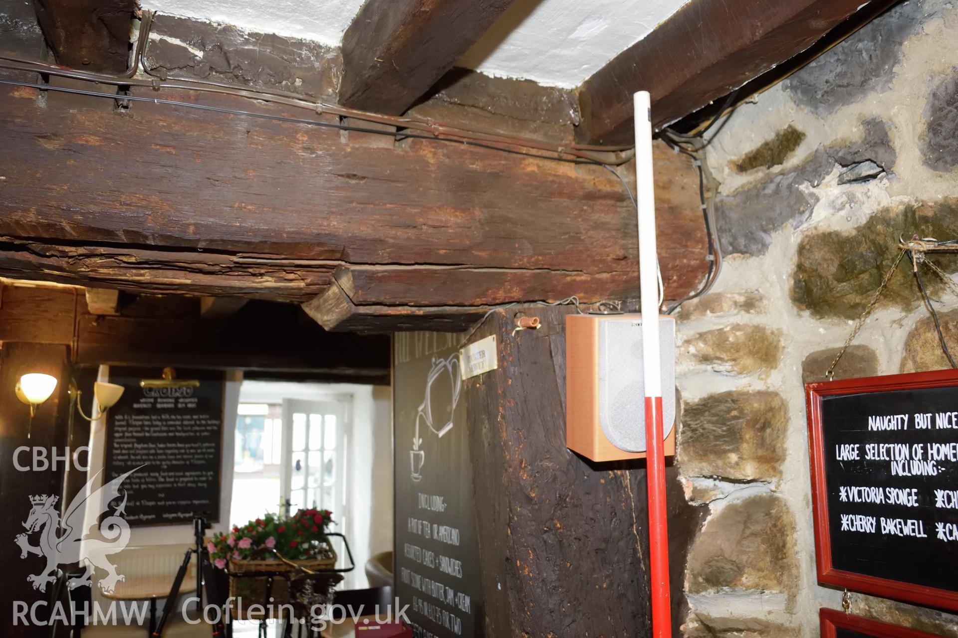 Colour photograph showing view looking east at post supporting a ceiling beam near to the fireplace at Y Sospan, Llys Owain, Dolgellau. Photographed by I. P. Brookes of Engineering Archaeological Services, June 2019.