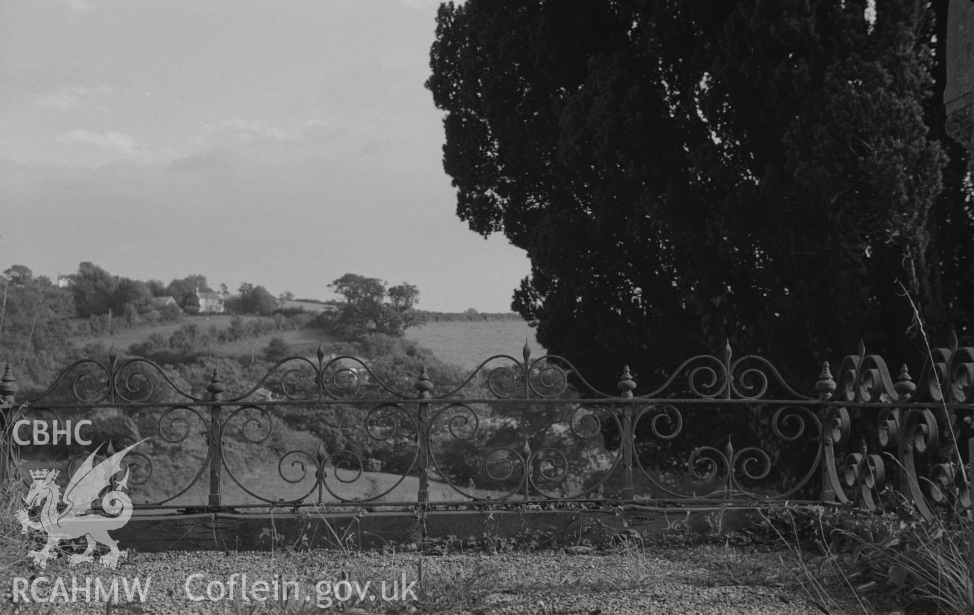Digital copy of a black and white negative showing wrought iron work around a grave enclosure in graveyard at St. Tygwydd's church, Llandygwydd, Cardigan. Photographed by Arthur O. Chater in September 1966 looking south from Grid Reference SN 242 438.