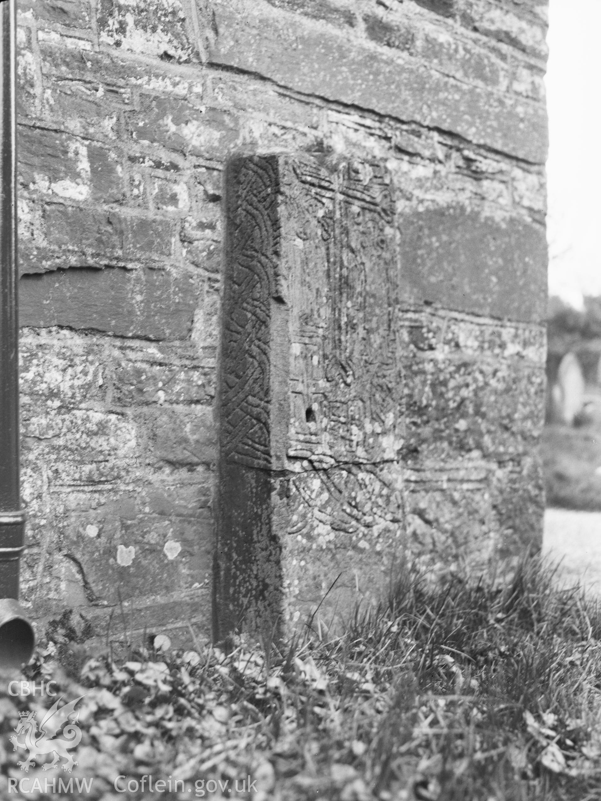 Digital copy of a nitrate negative showing exterior view of Cross-slab outside the wall of Llanhamlach Church.  The stone was taken inside the church. From the National Building Record Postcard Collection.