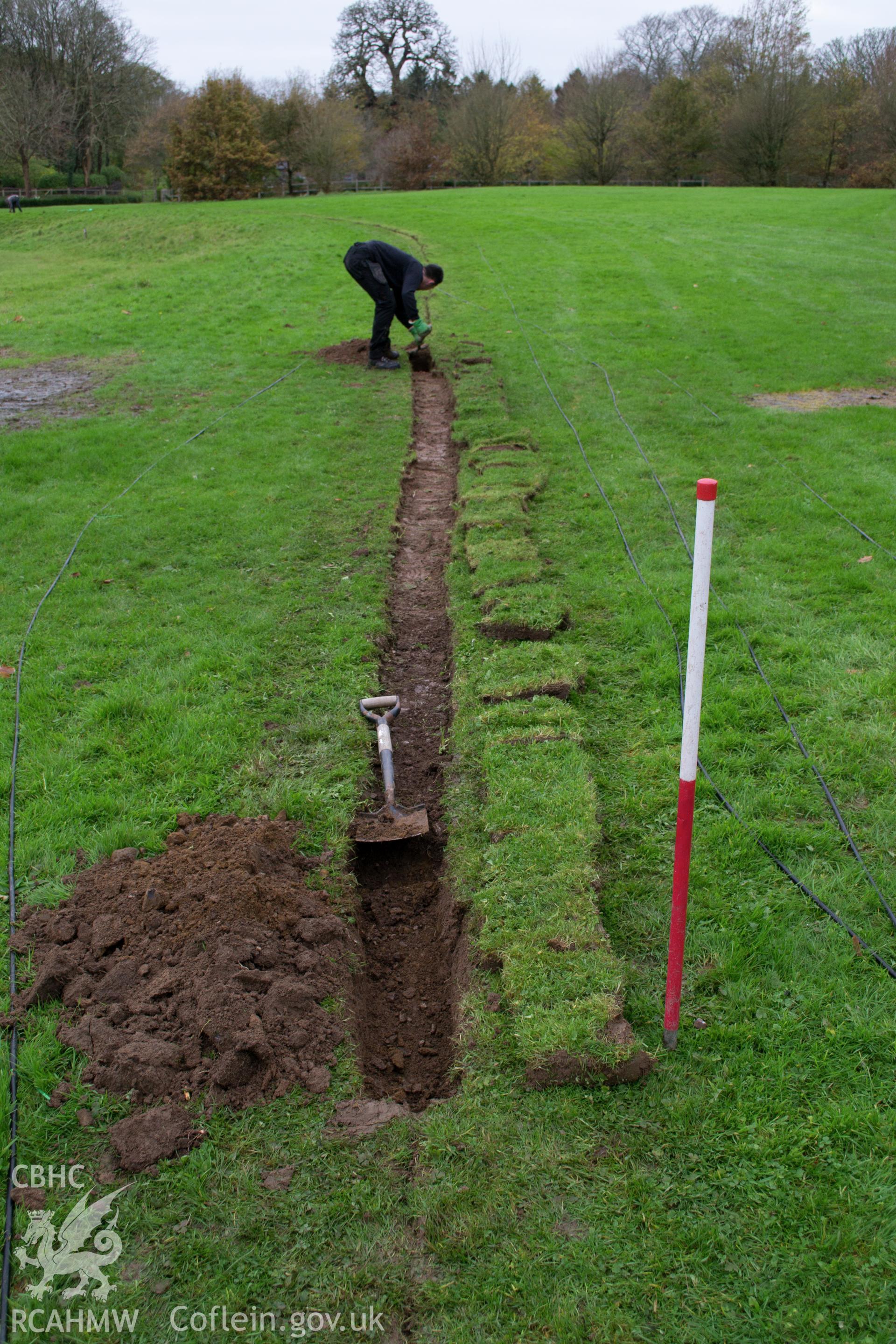 Action shot view from the east of reduction of 10m length to a 0.40m trench width. Photographed during archaeological watching brief of Plas Newydd, Ynys Mon, conducted by Gwynedd Archaeological Trust on 14th November 2017. Project no. 2542.