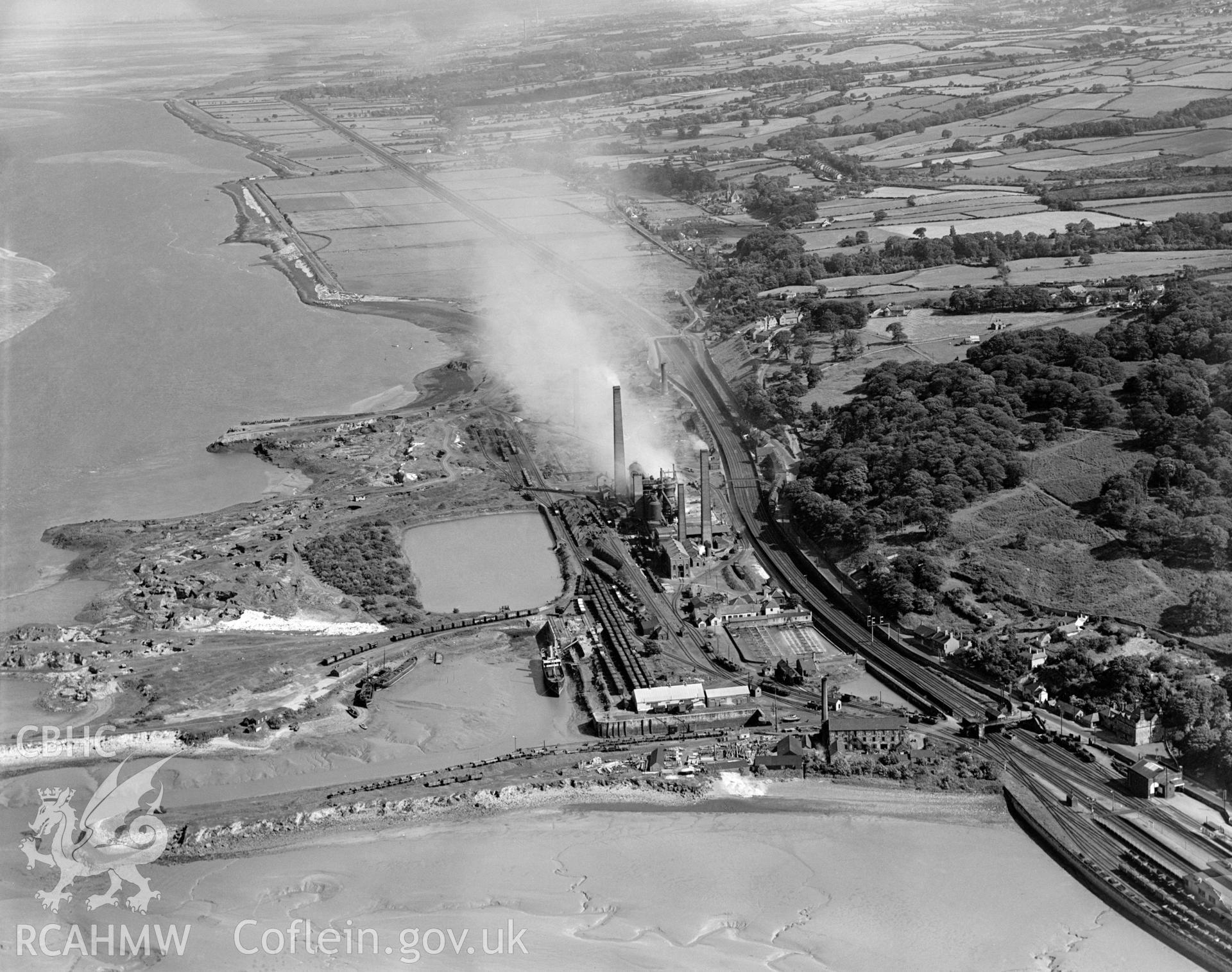 Digital copy of a black and white, oblique aerial photograph of Mostyn Quay. The photograph shows the view from the North West. Mostyn Quay saw a remarkable concentration of industry in one small area - there was a colliery, iron works, saw mill and oil works. The modern port of Mostyn was constructed upon an area of land reclaimed from the Dee estuary.