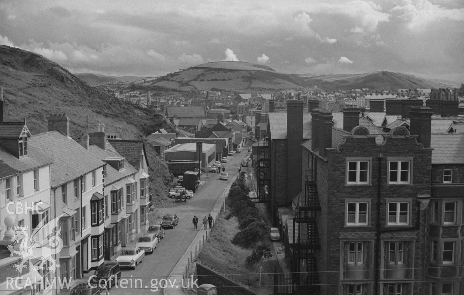Digital copy of a black and white negative showing views over Aberystwyth from the lower slopes of Constitution Hill with Alexandra Hall in the foreground. Photographed by Arthur O. Chater on 15th August 1967 looking south from Grid Reference SN 583 826.